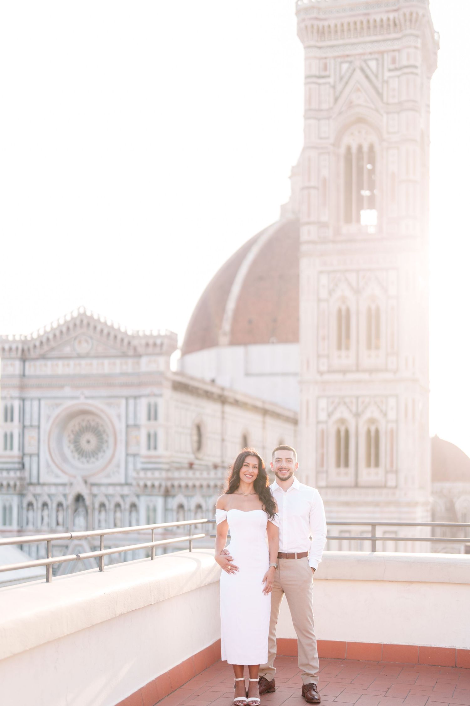 A couple embraces on a rooftop terrace overlooking the Florence Cathedral during golden hour in Italy.