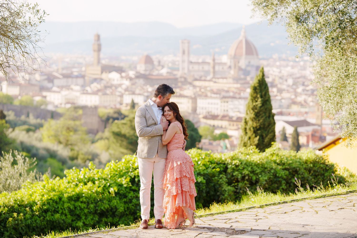 A couple in pink outfits enjoying a panoramic view of Florence, Italy with the iconic Duomo cathedral visible in the distance.