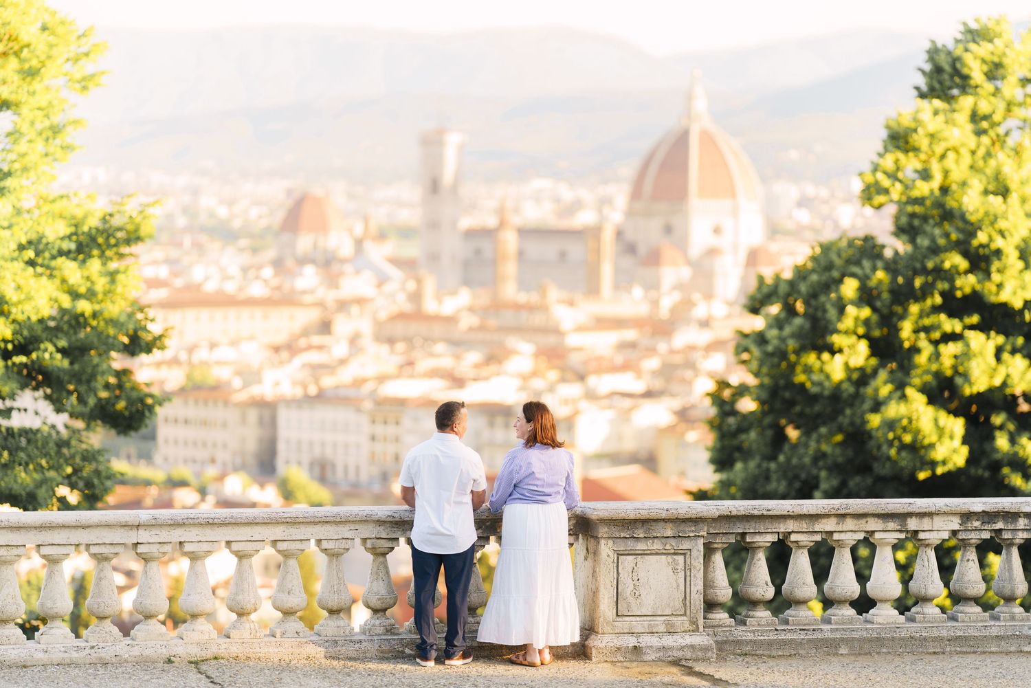 Couple enjoying scenic view of Florence, Italy from Piazzale Michelangelo during golden sunset hour.