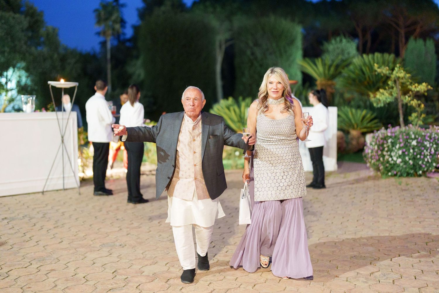 Wedding guests in formal attire walking along stone pathway at outdoor venue.