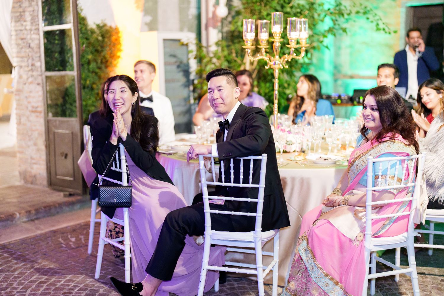 Wedding guests seated at decorated tables in an outdoor venue with soft ambient lighting.