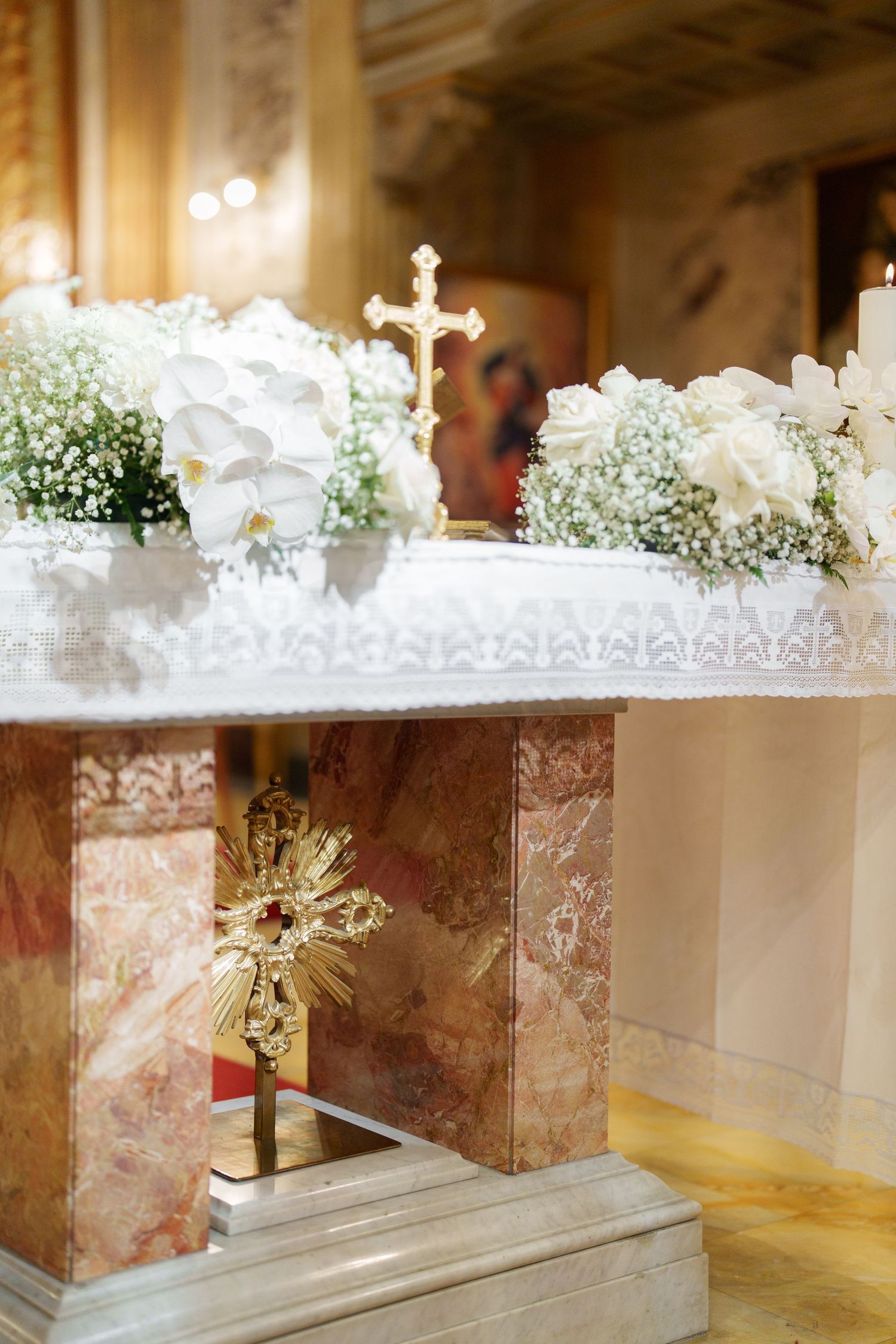 White floral arrangements with baby's breath decorate a marble altar in an elegant church setting.