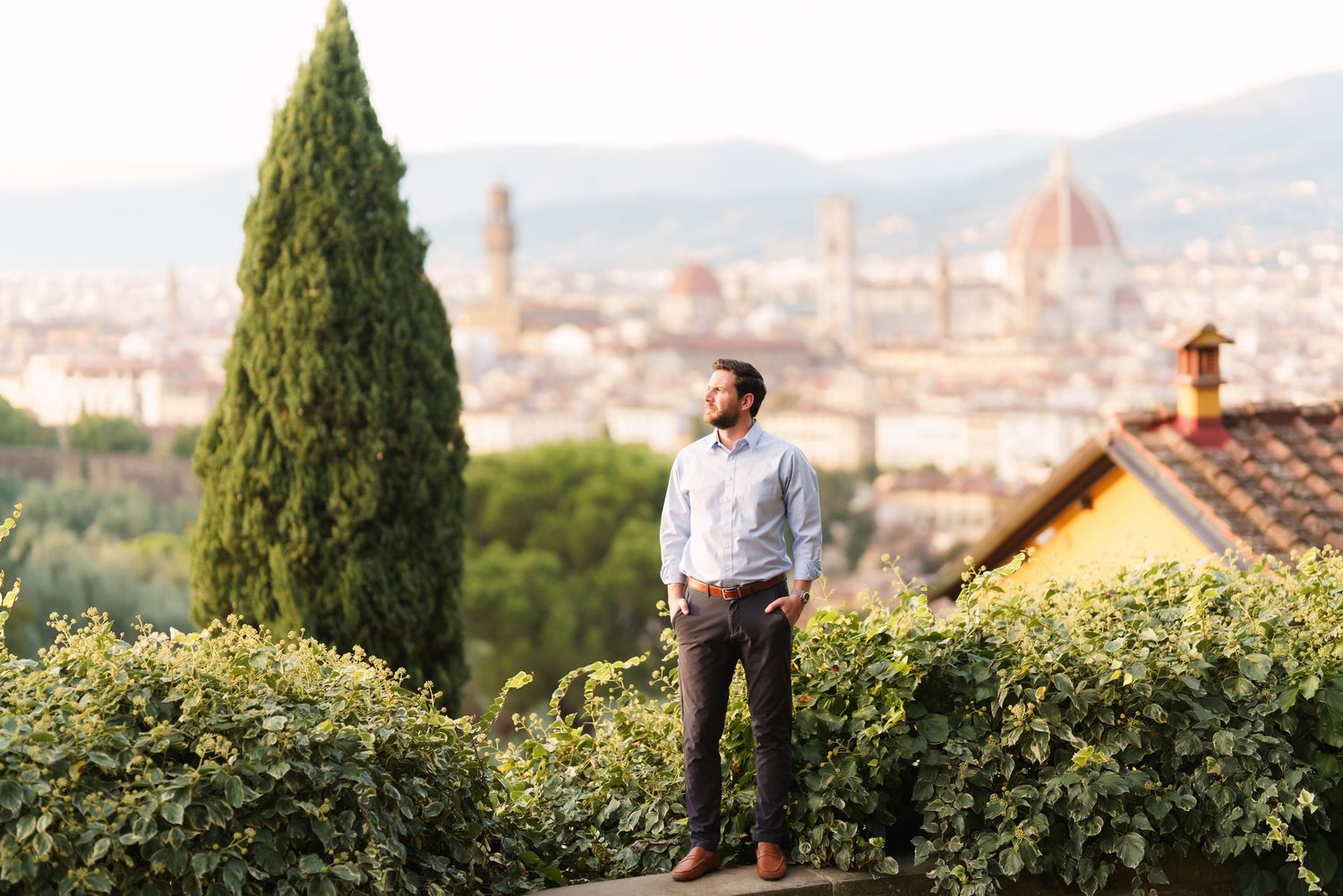 A panoramic view of Florence, Italy with the iconic Duomo cathedral and cypress trees in the foreground.