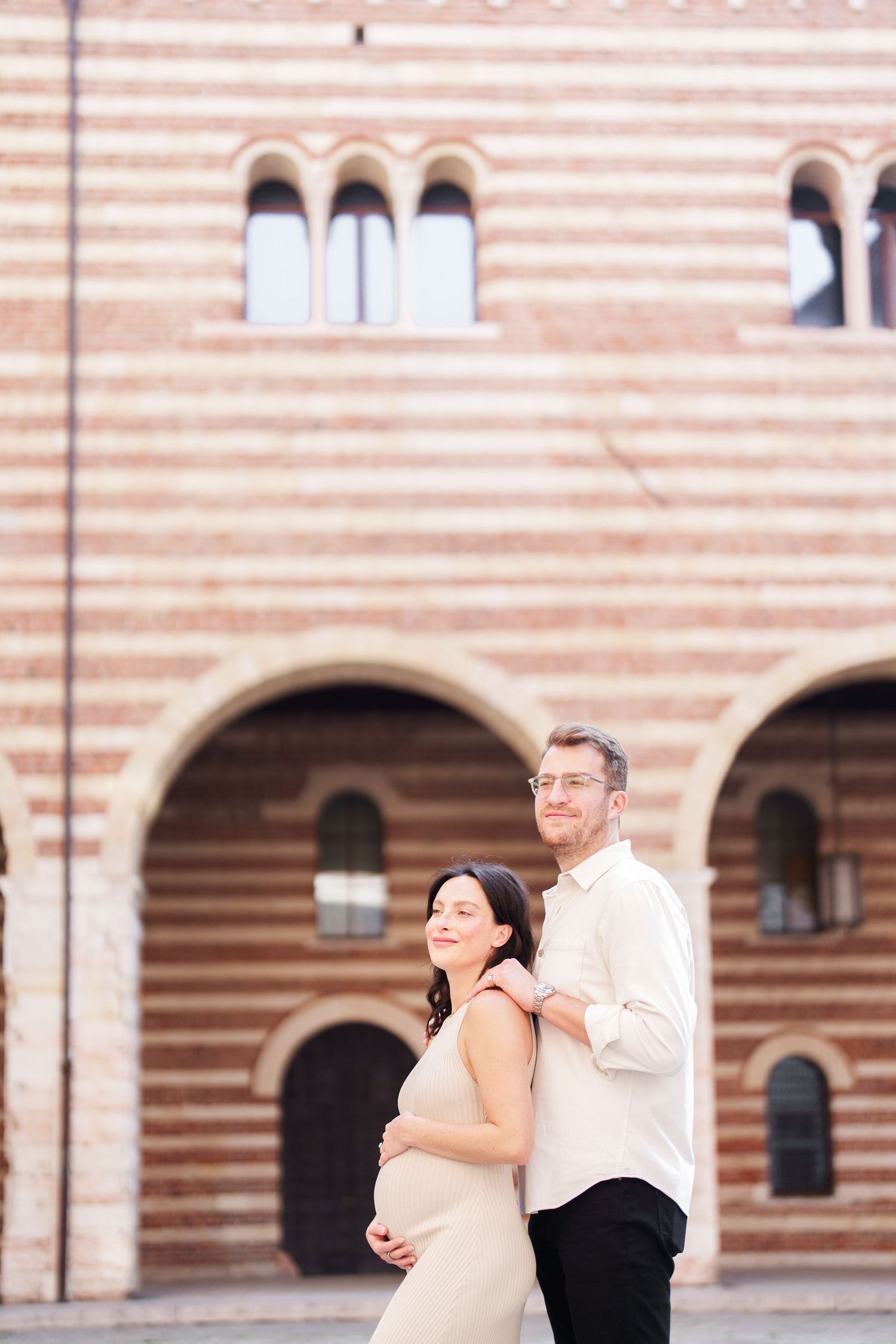 A couple dances together in front of a grand stone building with arched architecture.