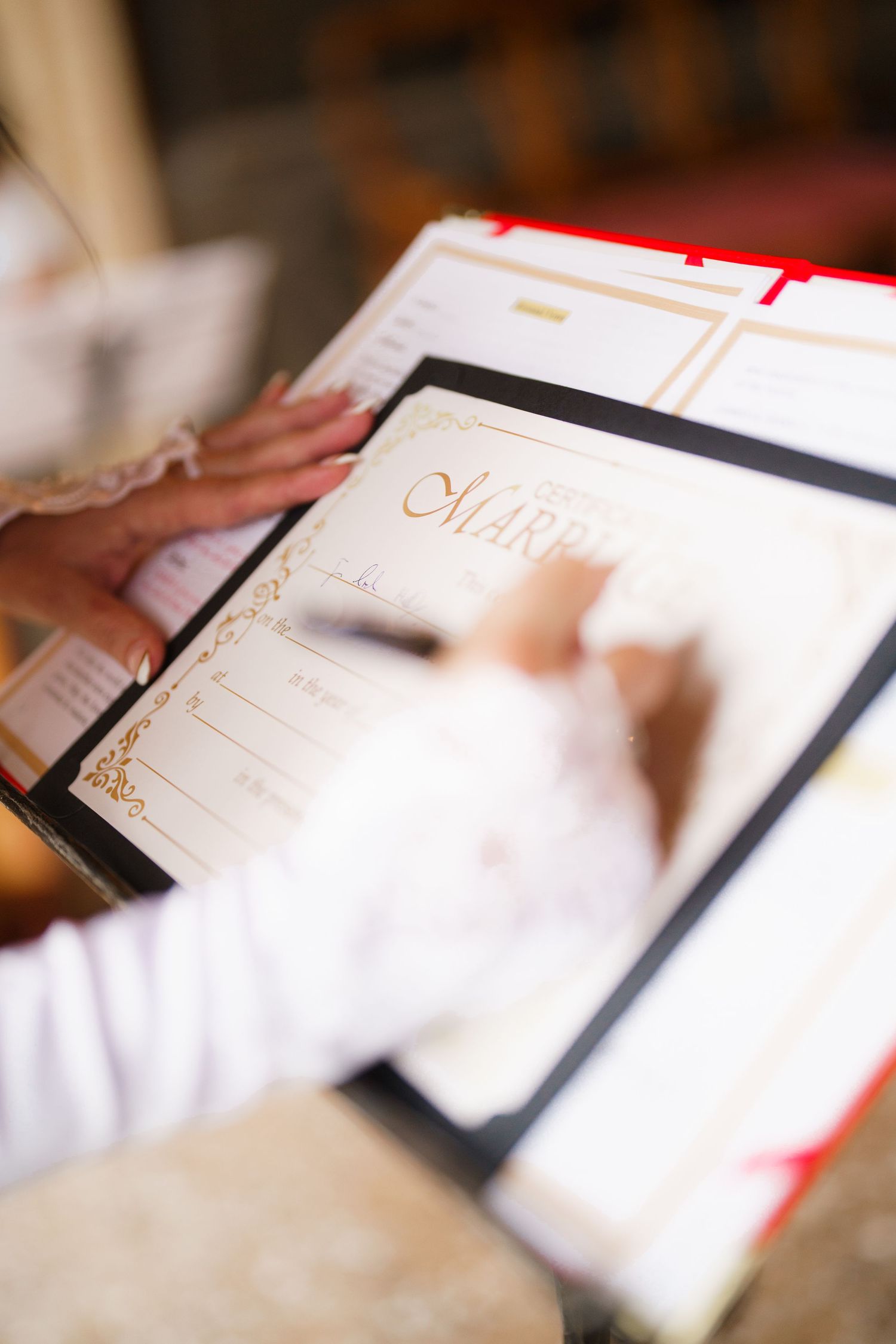 Someone signs an elegant wedding guest book with ornate gold details on white paper.