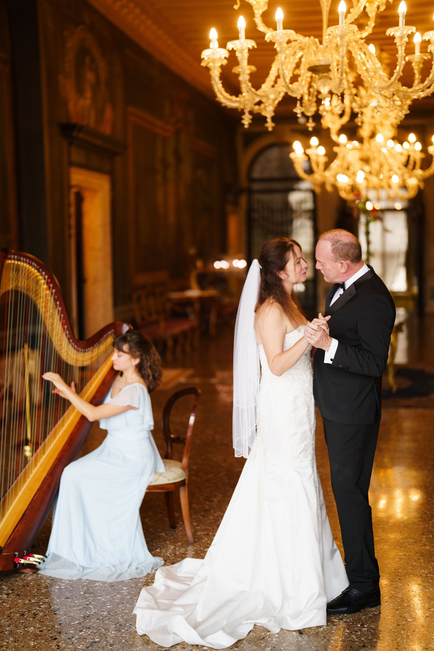 Romantic dance sequence under crystal chandeliers with bride in white gown and groom in black suit.