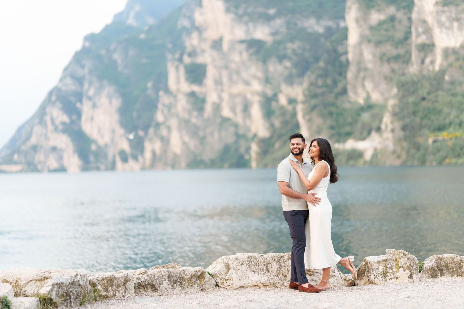 Couple enjoying a romantic moment along a scenic stone wall overlooking a misty mountain lake.