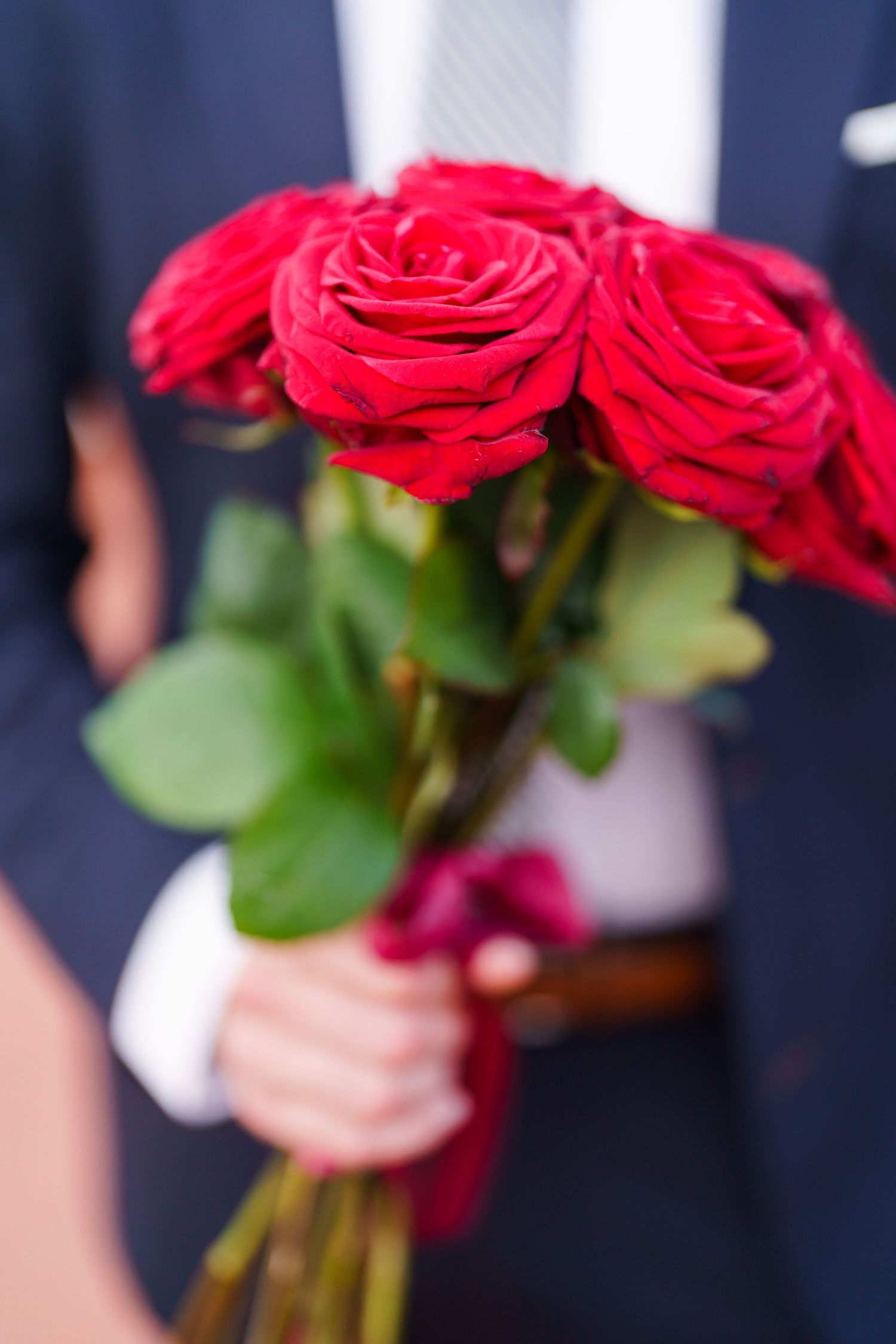 A person holding a bouquet of vibrant red roses against a dark background, showing only their hands and torso.