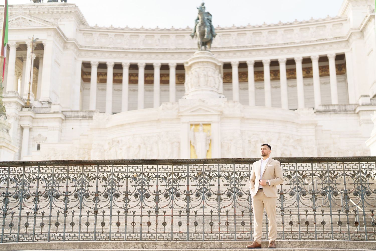 A well-dressed man in a beige suit stands before the grand Altare della Patria monument in Rome, Italy.
