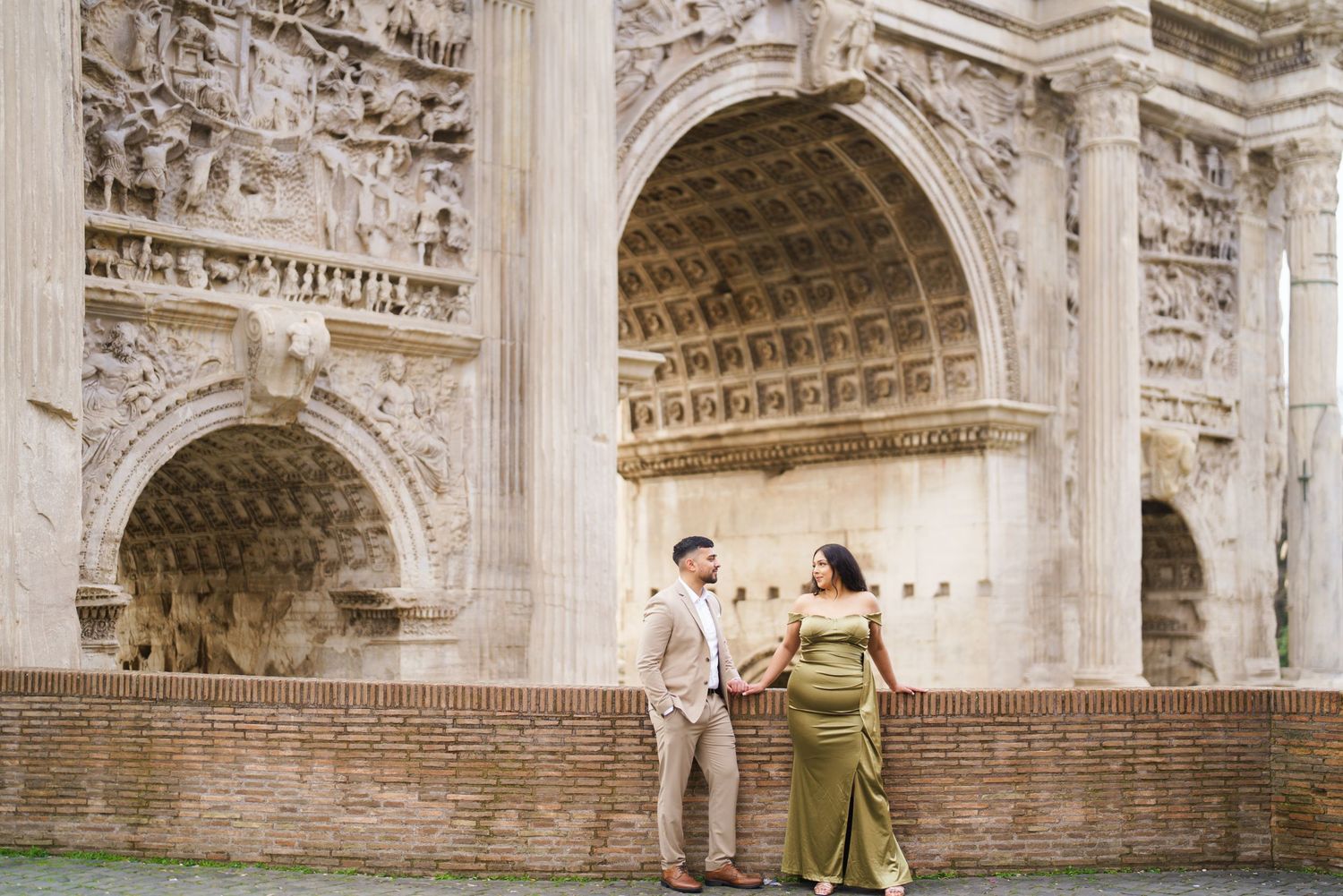 Couple posing in front of the Arch of Constantine in Rome, woman in green gown, man in beige suit.