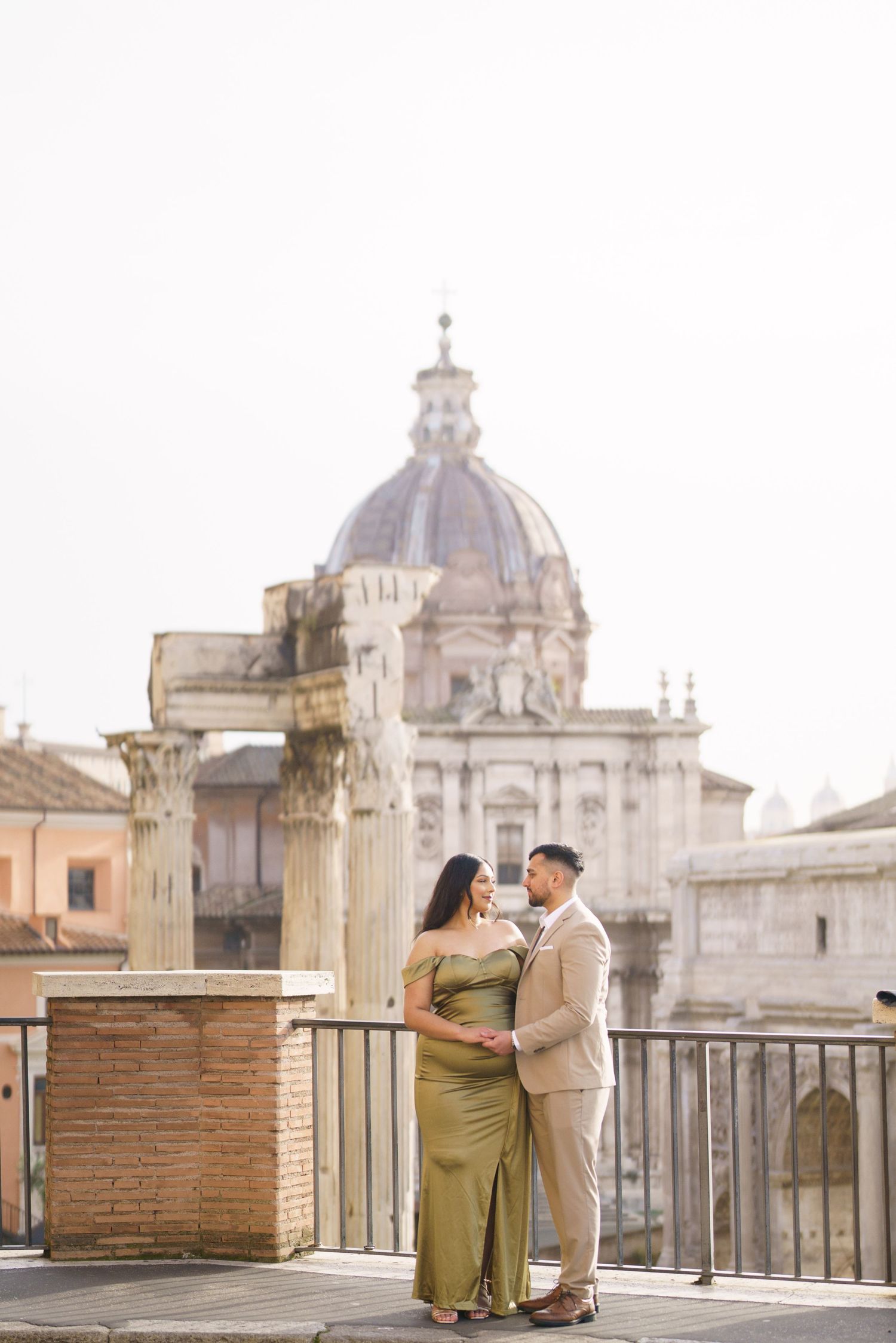 Couple posing on a rooftop terrace with Roman ruins and a domed church in Rome, Italy.
