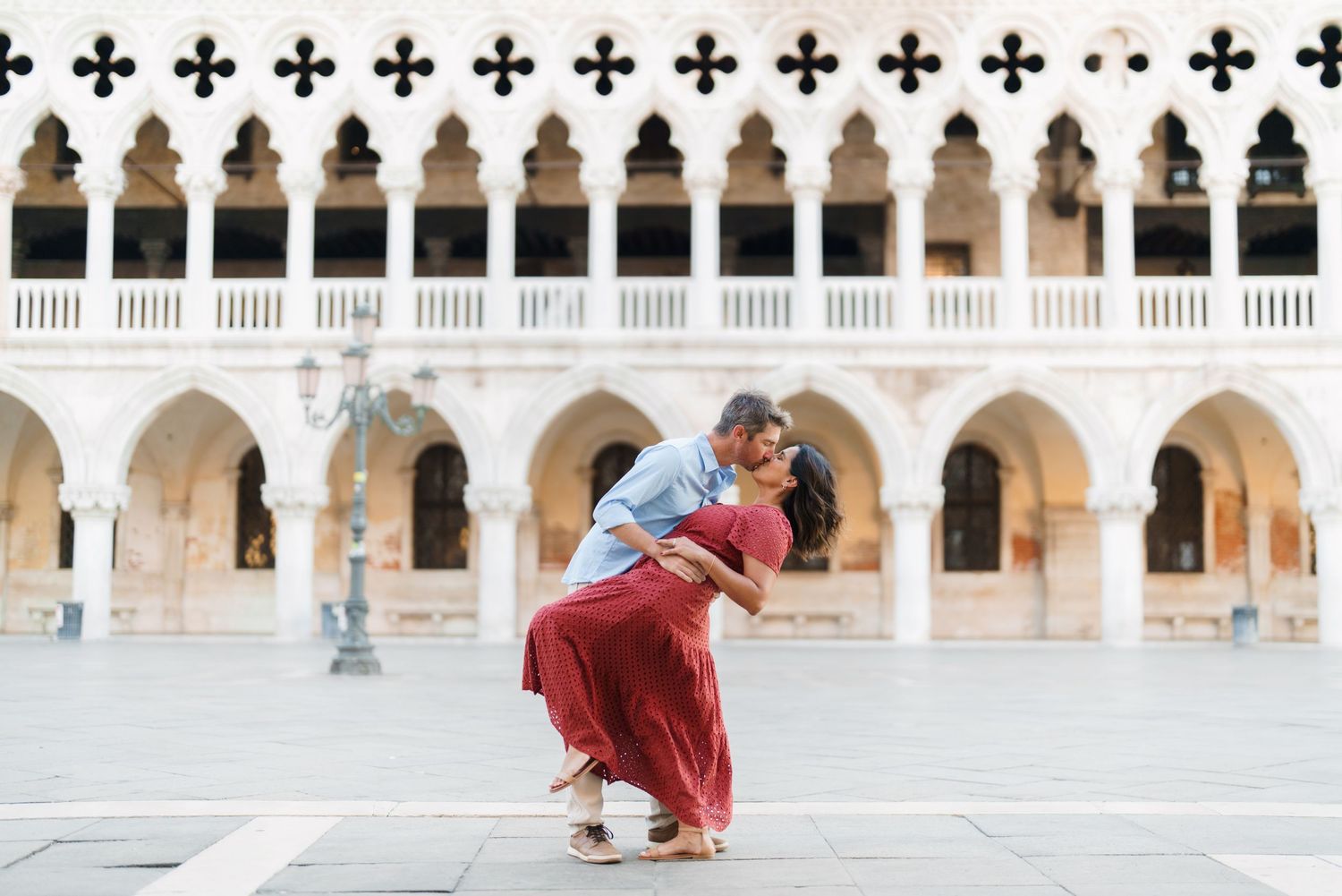 Romantic couple sharing a dip kiss in St. Mark's Square, Venice, with stunning Gothic arches in the background.