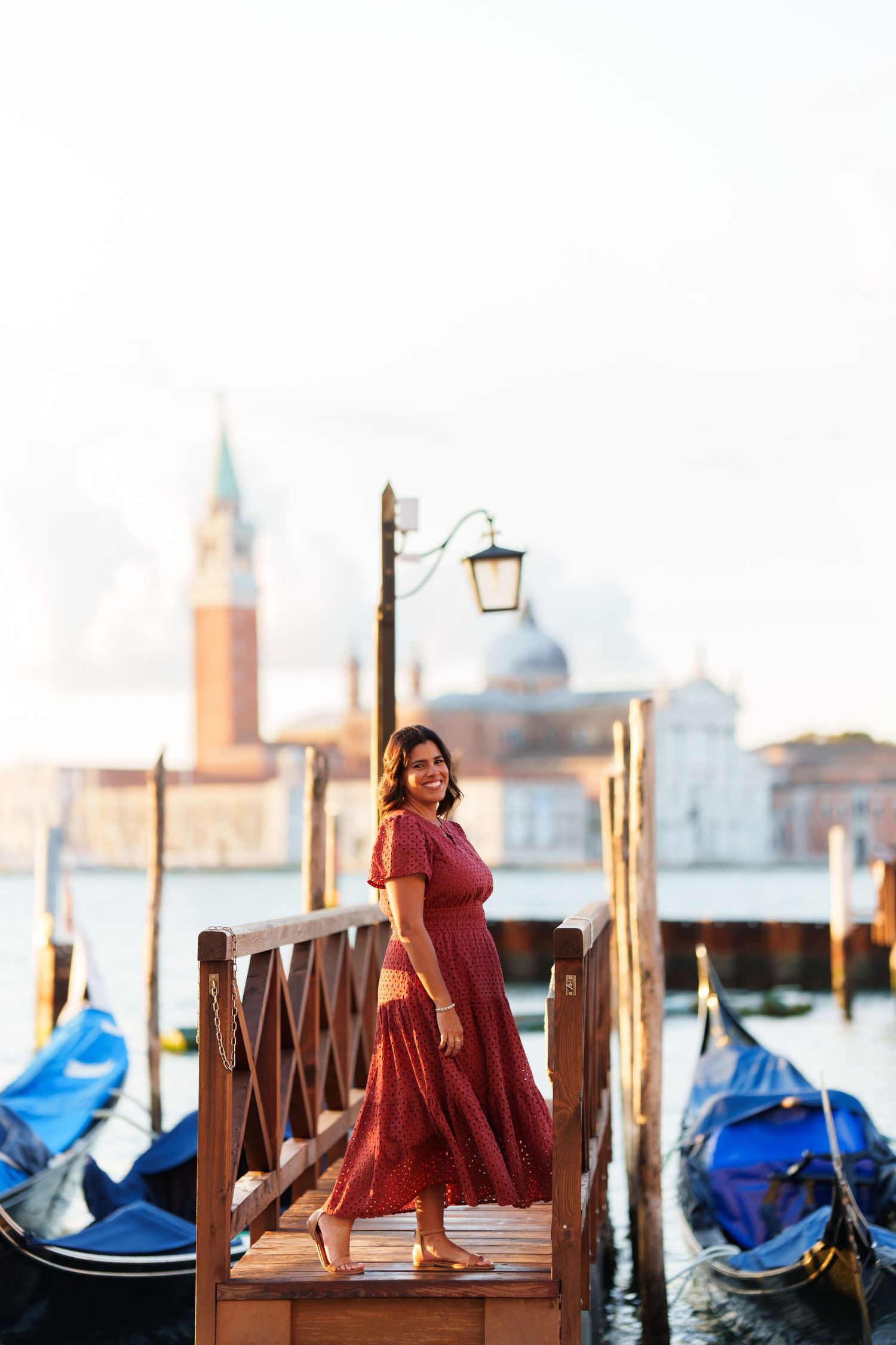 Woman in red dress standing on Venice gondola dock with San Giorgio Maggiore church in background.