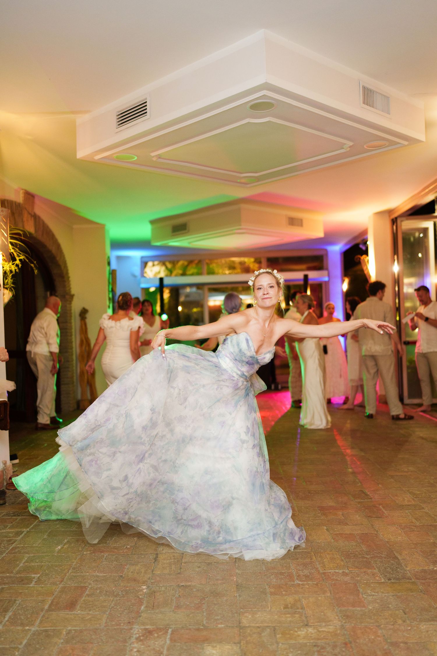 Bride in floral gown twirling gracefully on wedding reception dance floor with colorful lighting.