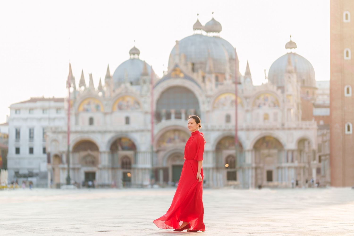 Woman in red gown poses in St. Mark's Square, Venice, with the iconic Basilica di San Marco in the background.