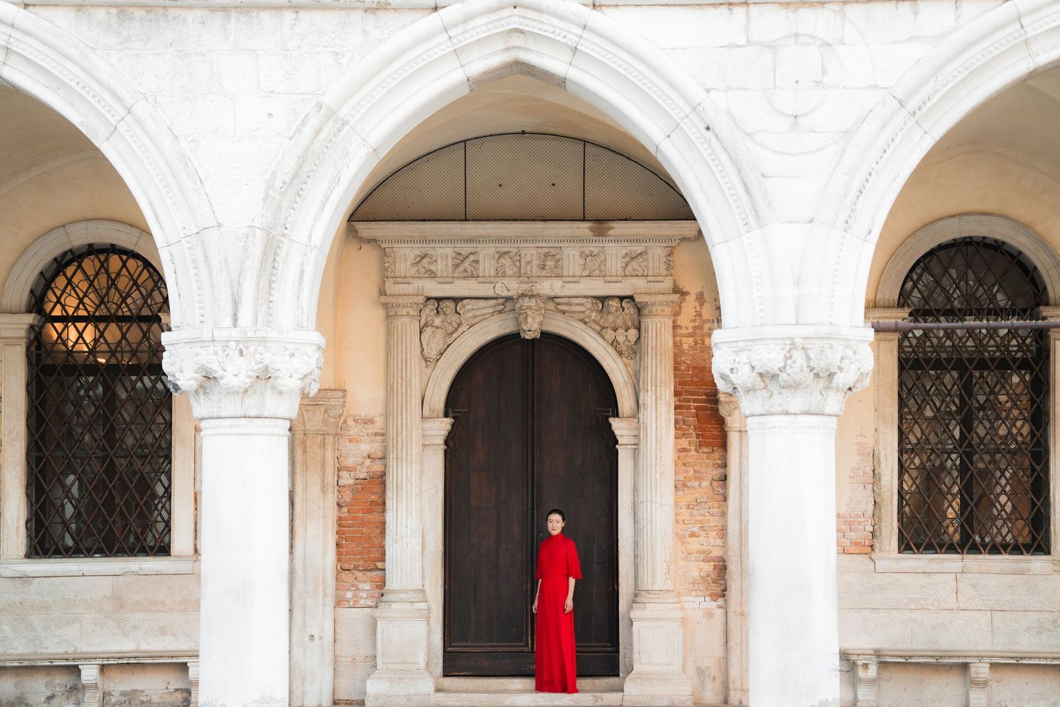 Woman in red dress standing in elegant white marble archway doorway in Venice, Italy.
