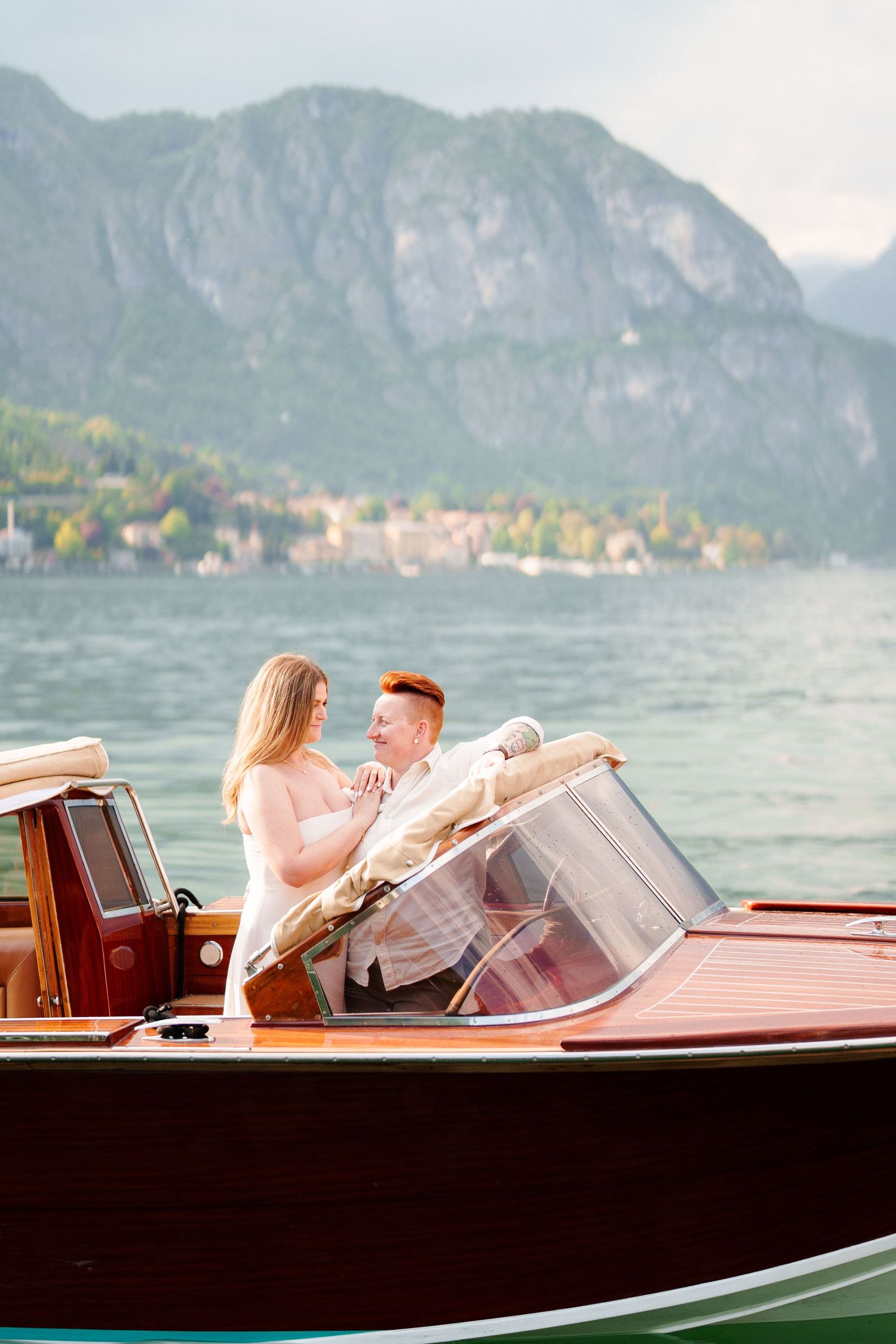 Couple sharing a romantic moment on a classic wooden boat with mountain lake backdrop.