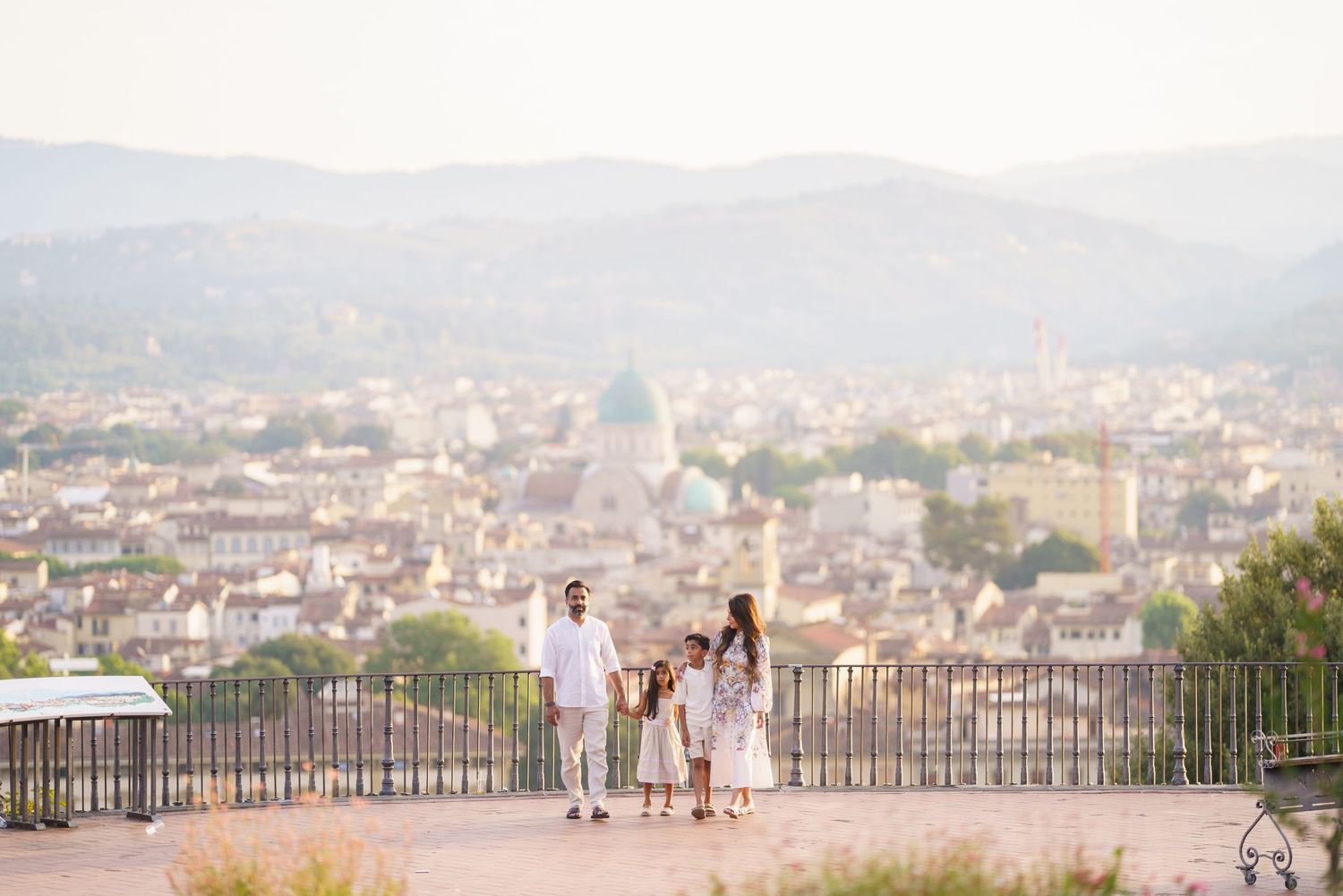 Family of four strolling on a hilltop terrace overlooking the scenic cityscape of Florence, Italy.