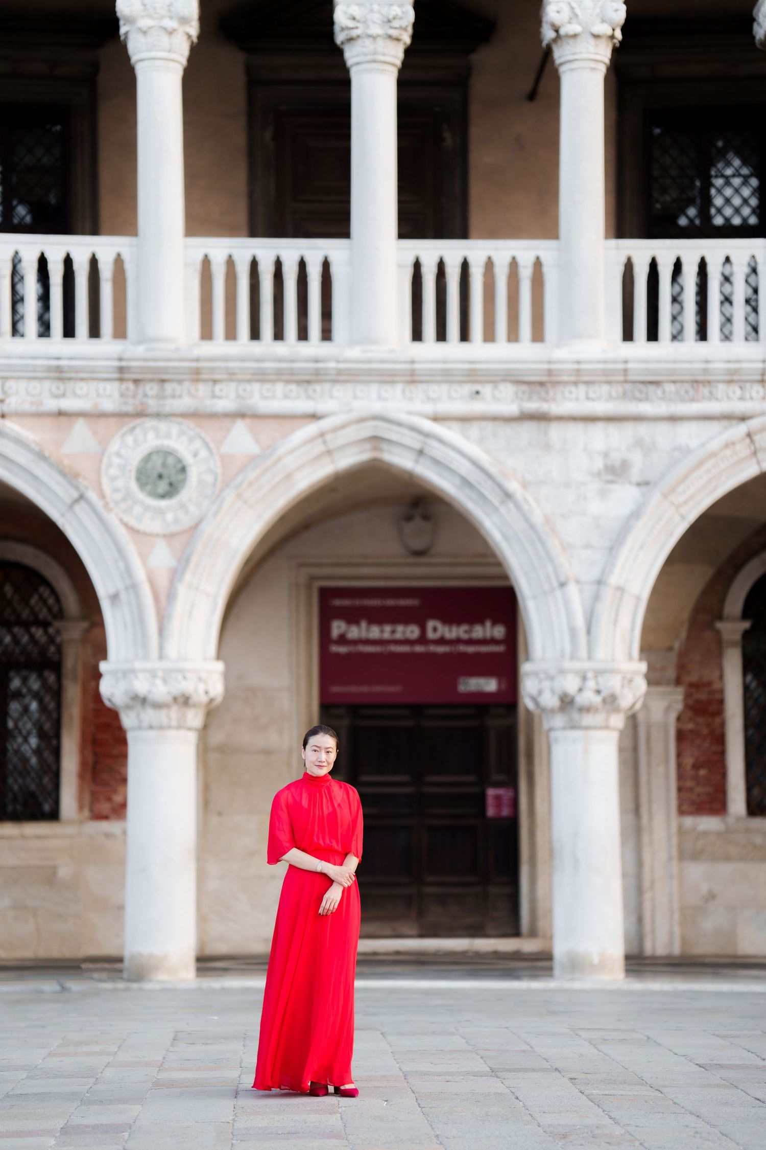 Woman in red dress standing before Palazzo Ducale Gothic arches in Venice, Italy.