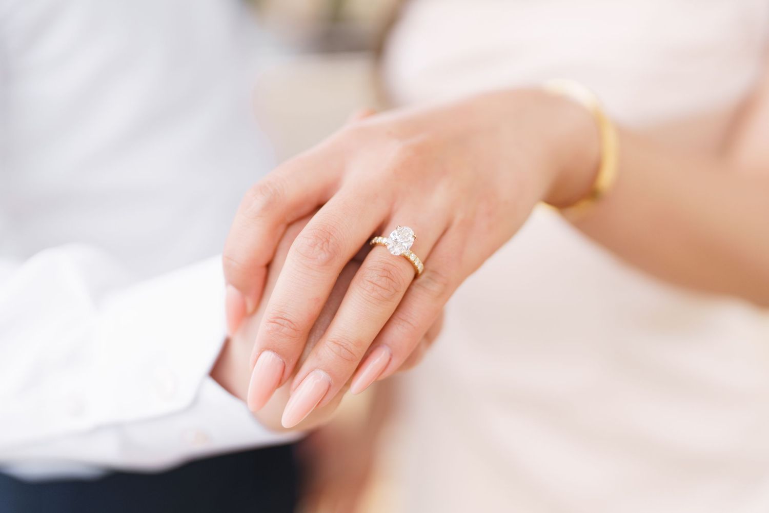 Close-up of a bride's hand wearing a diamond engagement ring and gold bracelet resting on a groom's sleeve.