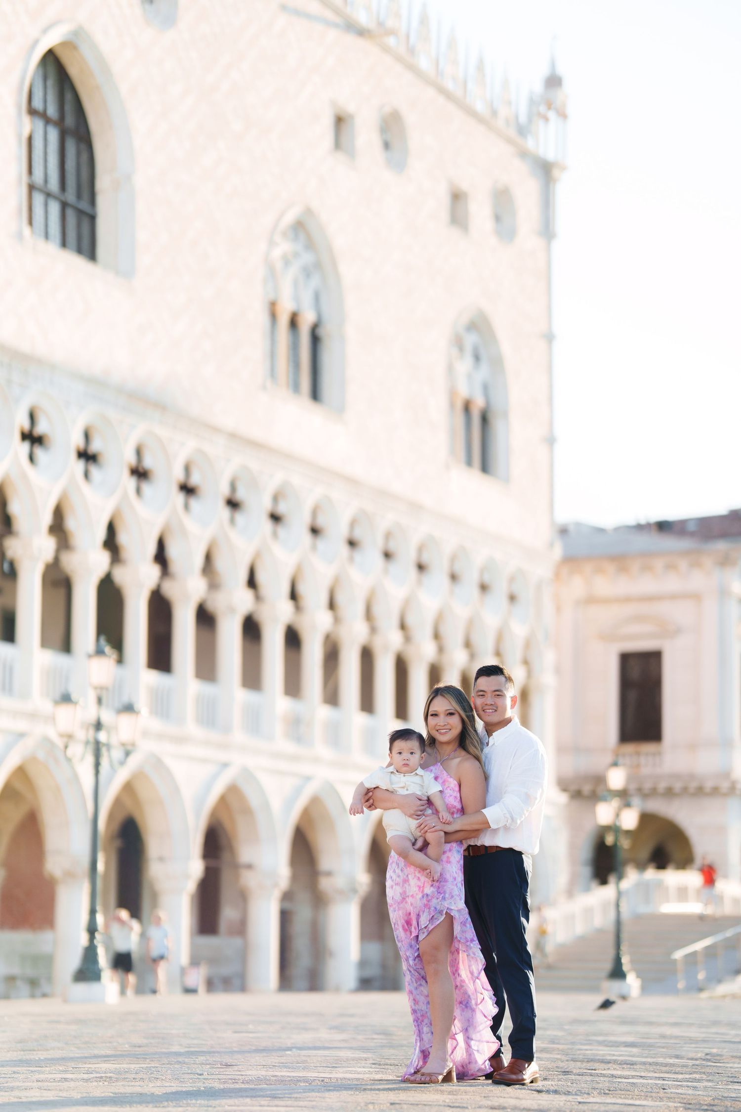 Family posing in front of the Doge's Palace in Venice, Italy, with a woman in a pink dress holding a baby.