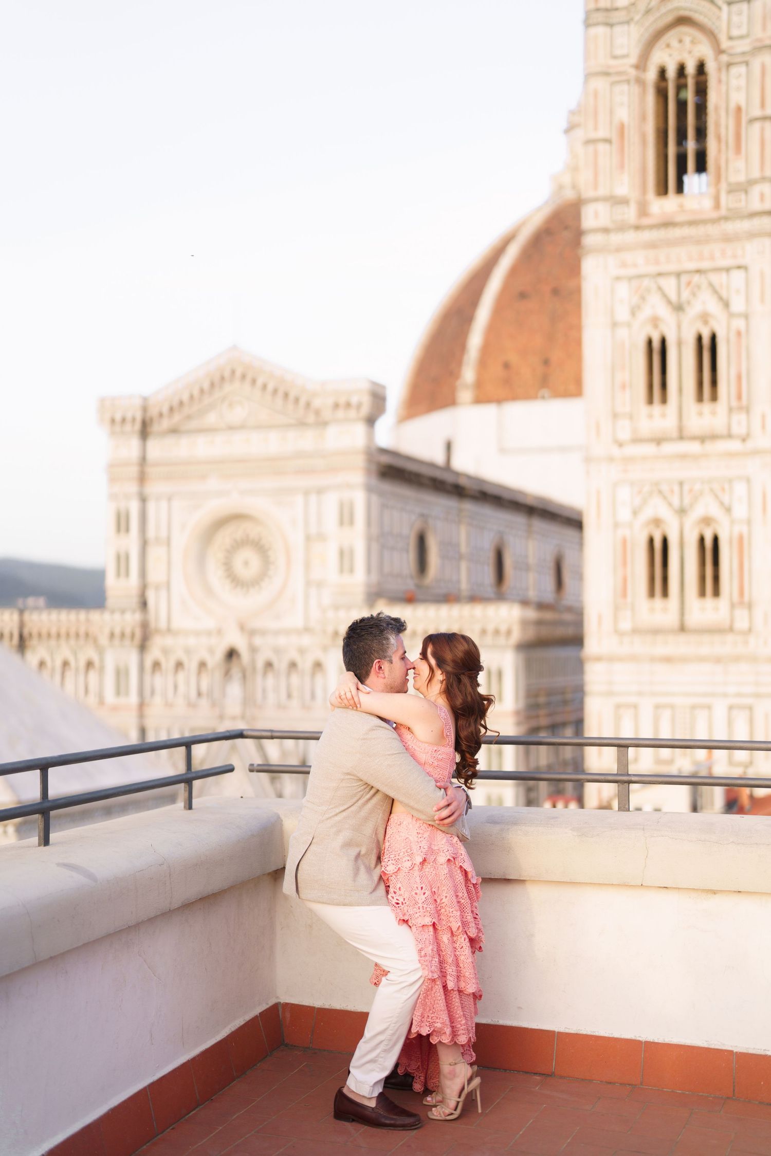 A romantic couple embraces on a rooftop terrace with Florence Cathedral's iconic dome and architecture in the background.