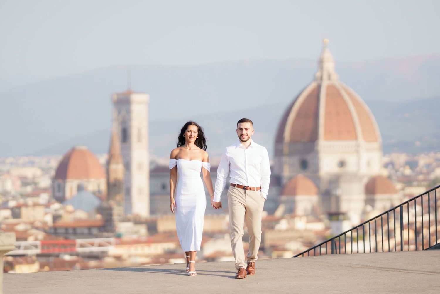 Couple walking hand in hand on a scenic overlook with Florence's iconic Duomo cathedral in the background.