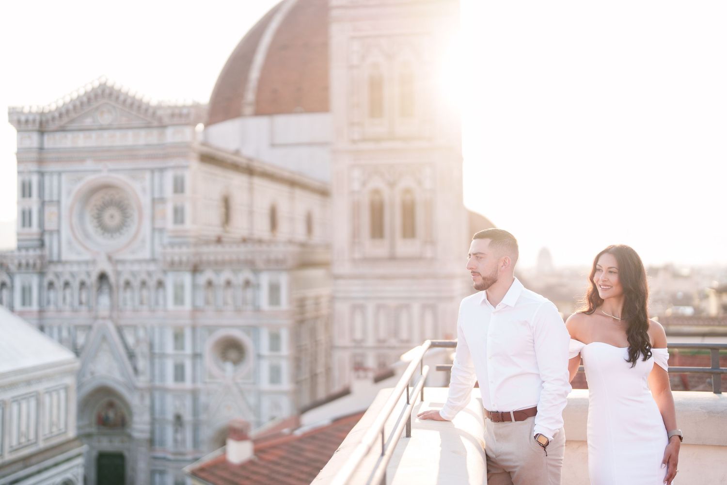 A couple in wedding attire embraces on a balcony overlooking Florence's Duomo cathedral at sunset.