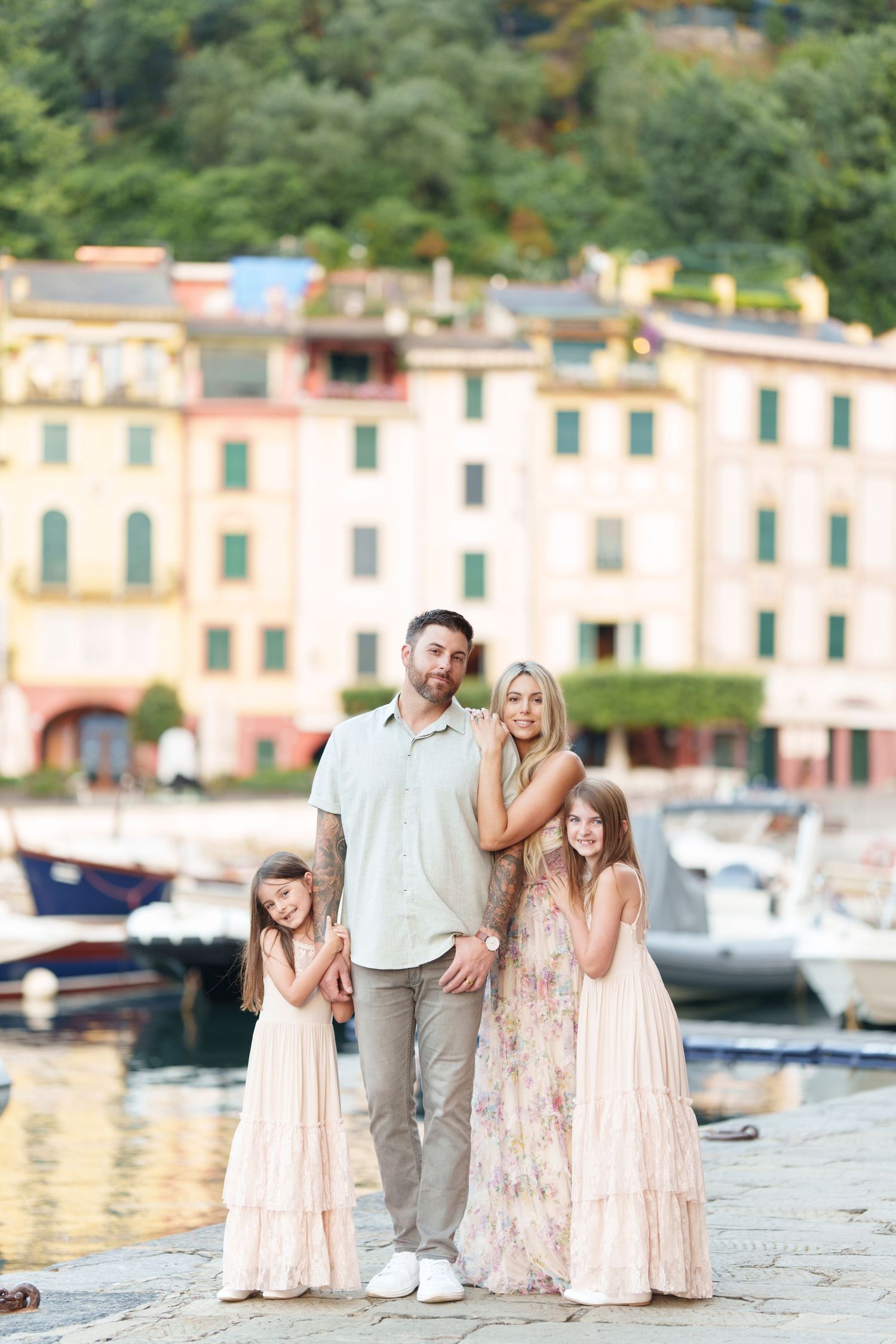 Family enjoying a scenic moment together by a Mediterranean harbor with boats and colorful buildings in the background.