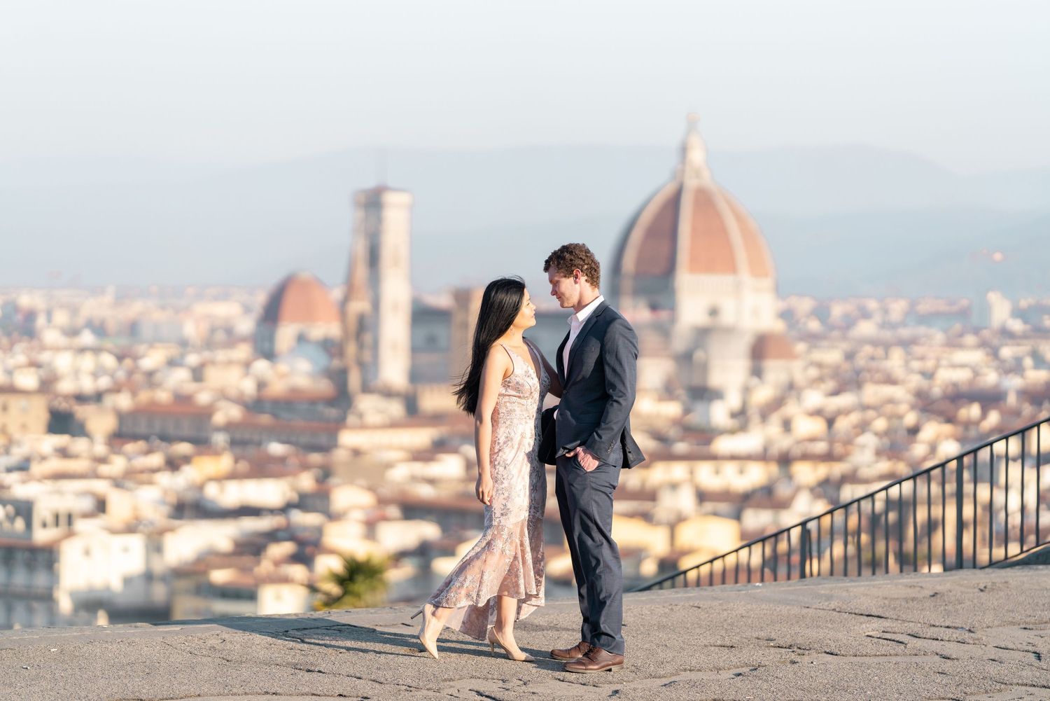 A couple poses romantically against the stunning backdrop of Florence, Italy with the iconic Duomo cathedral visible.