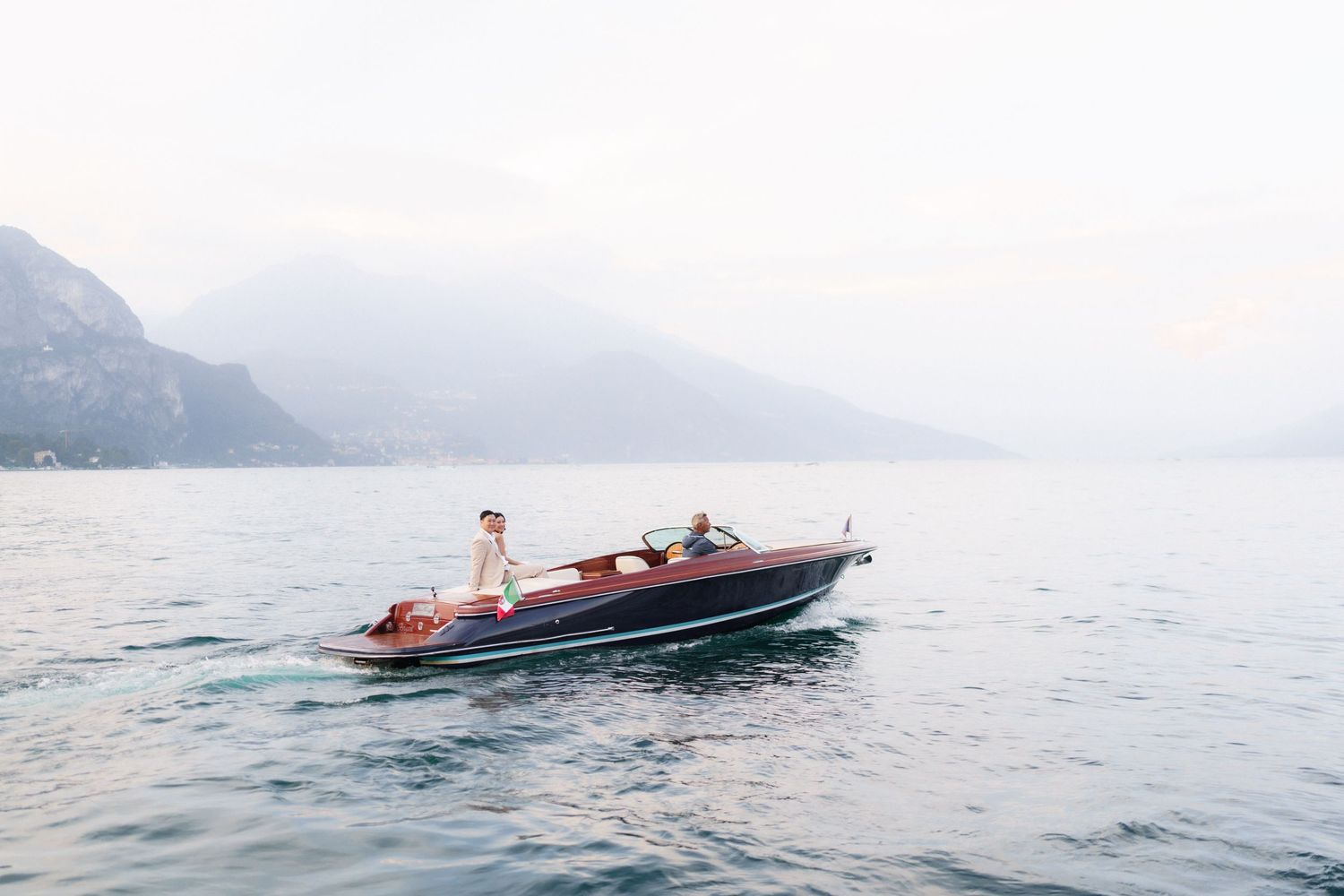 Vintage wooden boat glides across serene mountain lake on a misty summer morning.