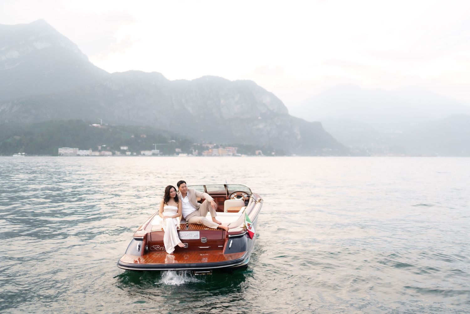 A wooden boat glides across a misty lake surrounded by mountains on a tranquil morning.