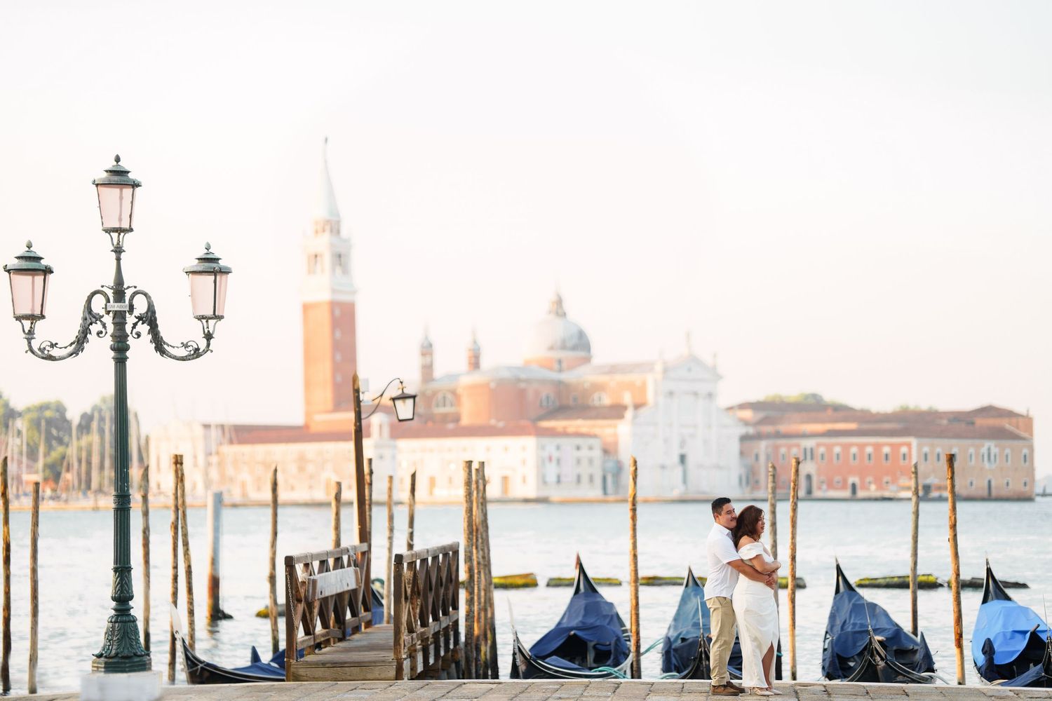 Ornate lampposts and gondolas line the Venice waterfront with the iconic San Giorgio Maggiore church in the background.
