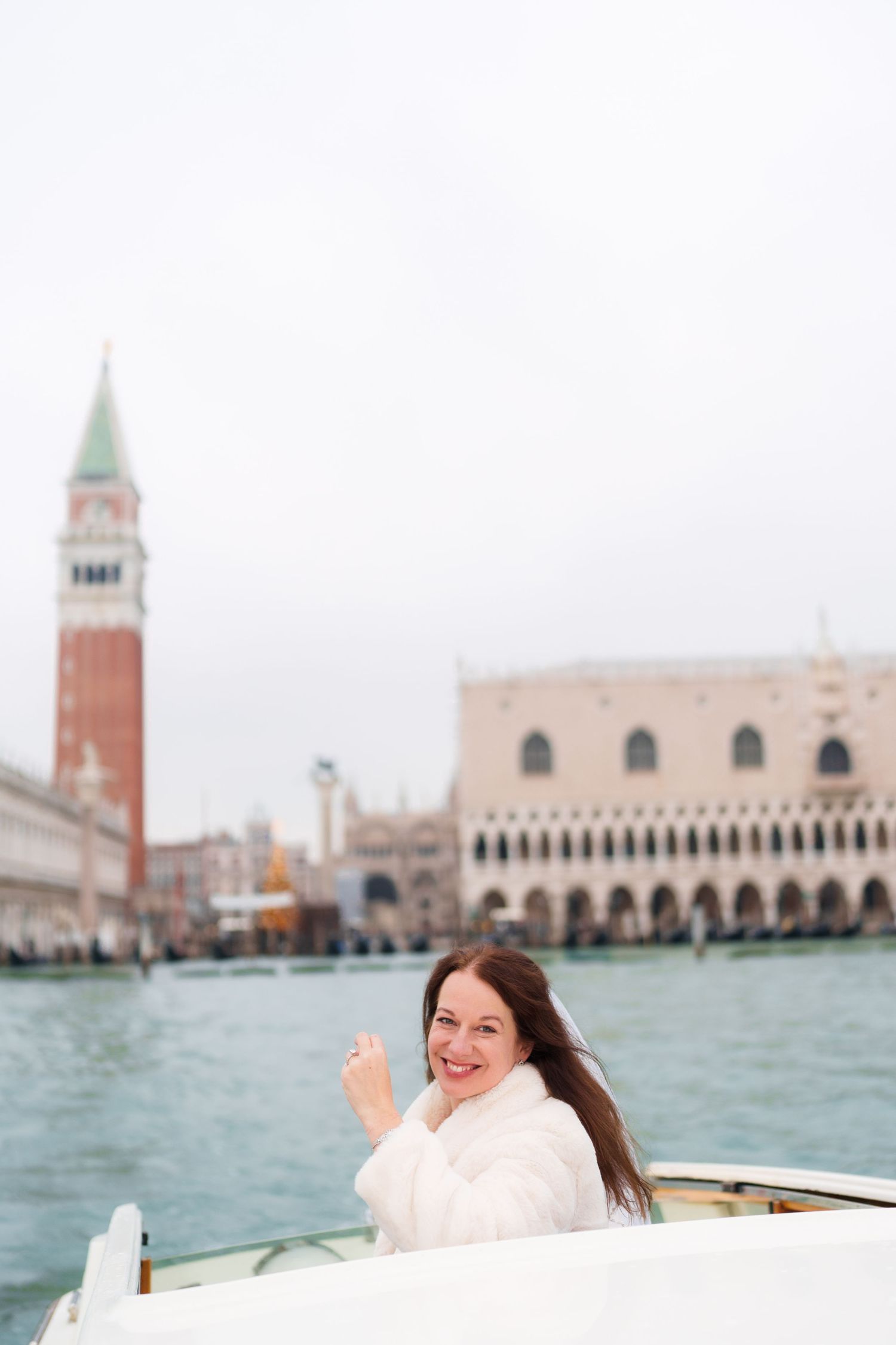 A scenic view of Venice's St Mark's Square and Campanile tower seen from a boat on turquoise waters.