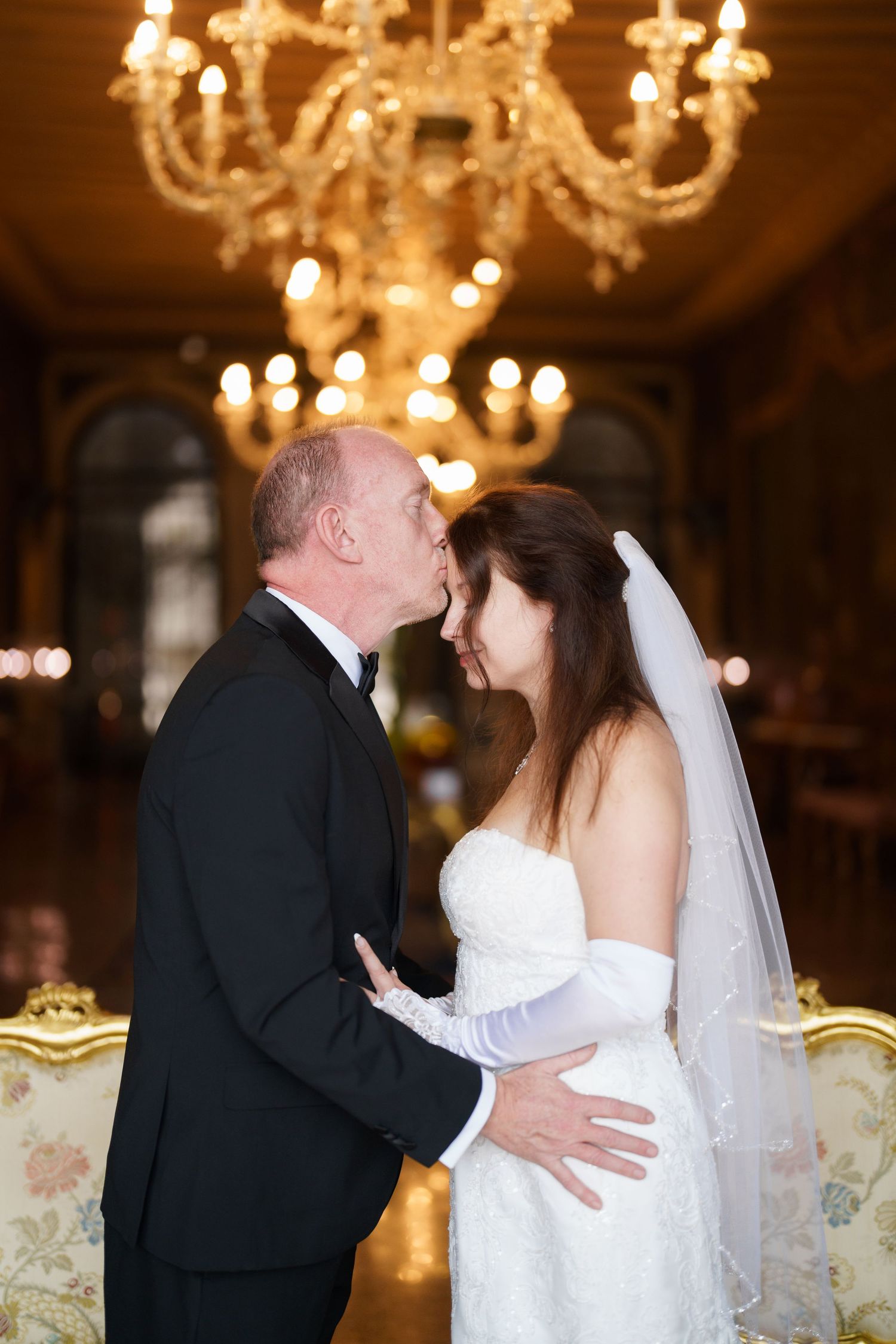 A romantic wedding kiss sequence captured under elegant chandeliers in an ornate ballroom setting.