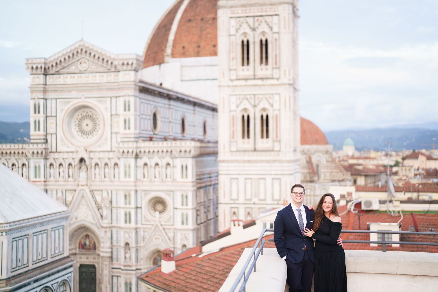 Couple poses on rooftop terrace overlooking Florence Cathedral and cityscape in Italy.