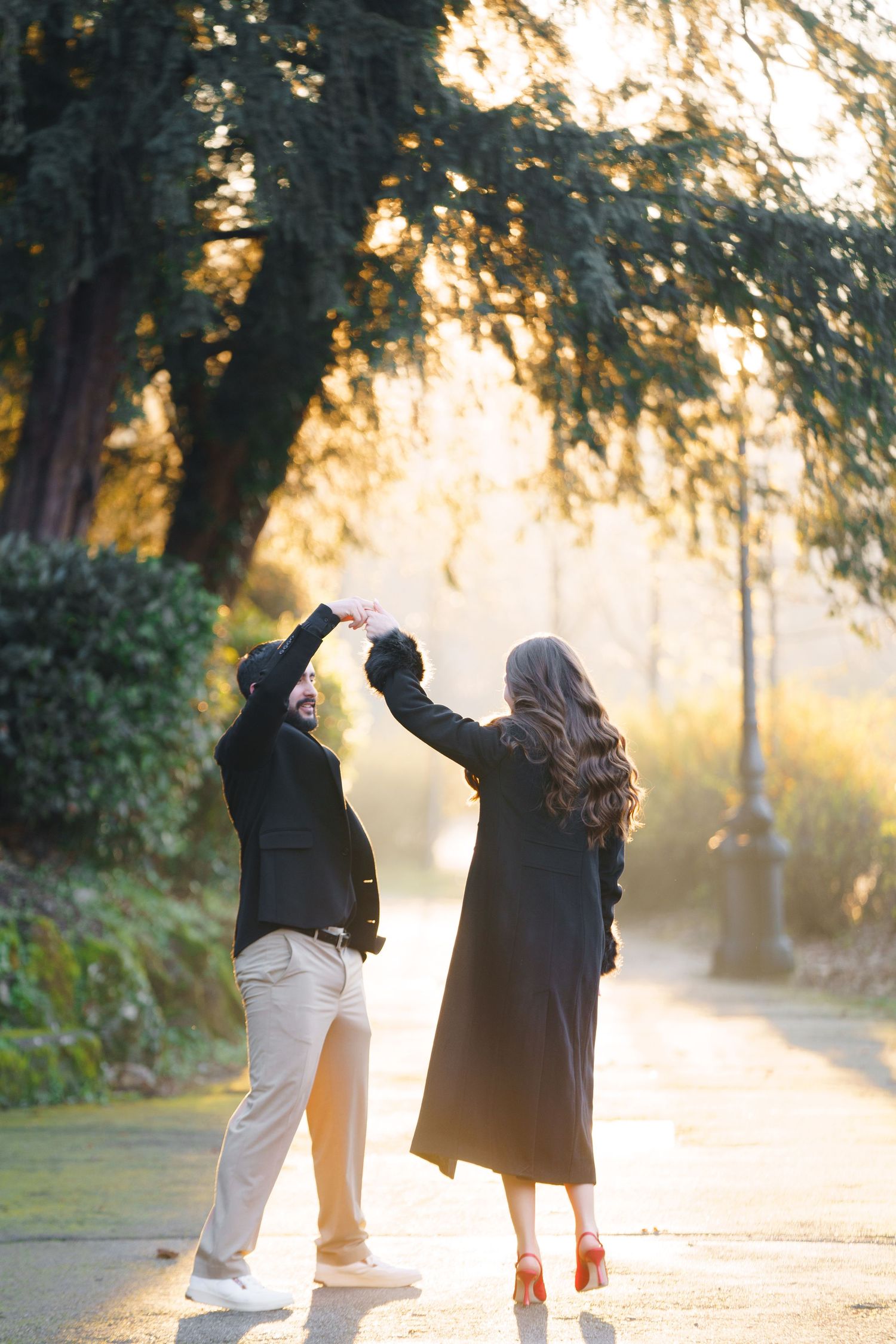 A couple dances together on a sunlit path in the park during golden hour with trees creating a magical backdrop.
