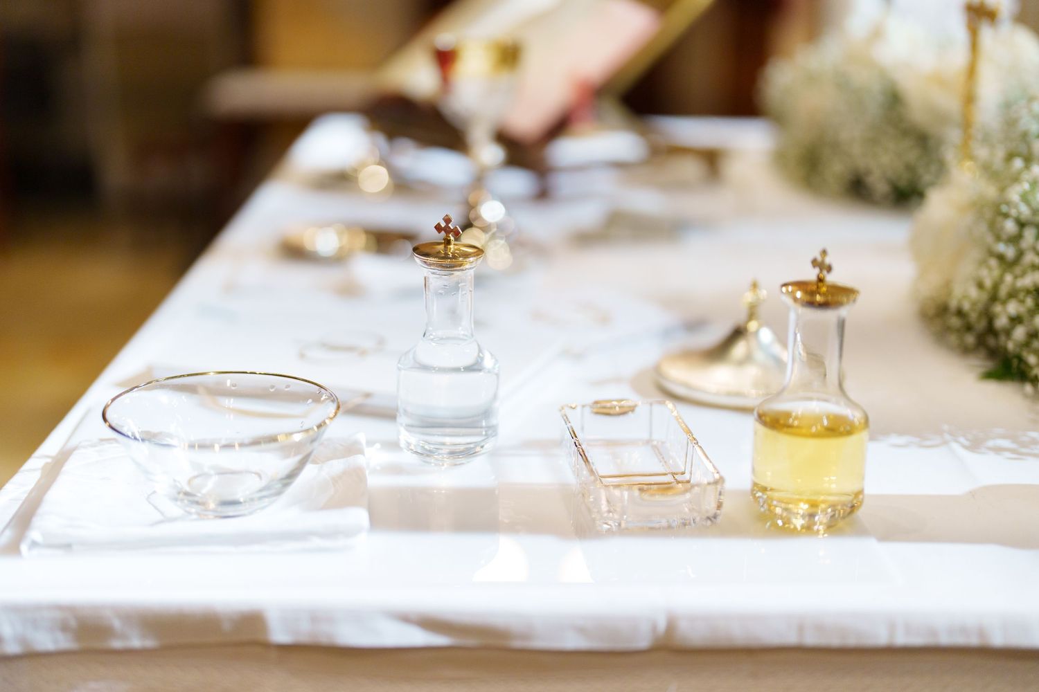 Holy water and oil vessels arranged on white linen during a religious ceremony.