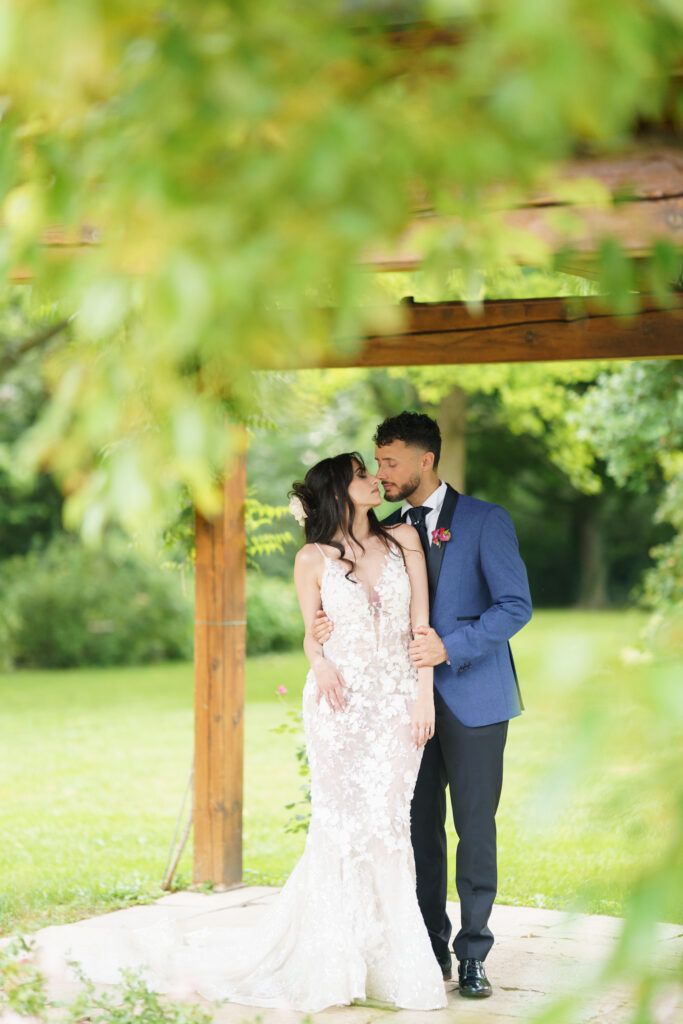 Garden wedding photoshoot under wooden pergola with lush green foliage.