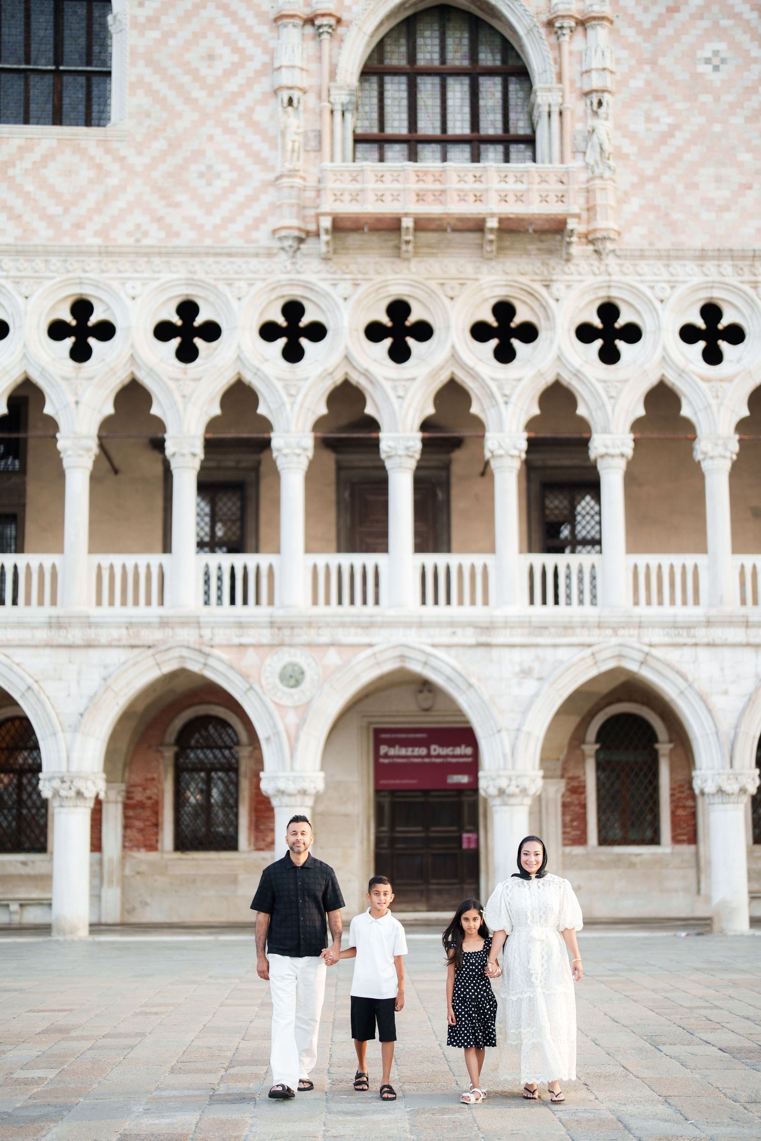 Family of four posing in front of the ornate Gothic facade of Palazzo Ducale in Venice, Italy.