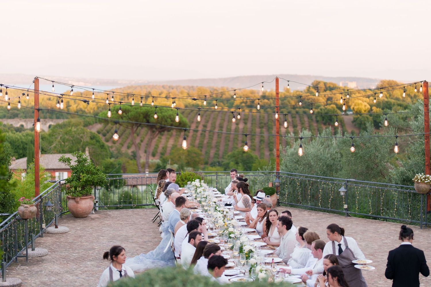 Outdoor wedding reception with long table, string lights, and vineyard views at sunset.