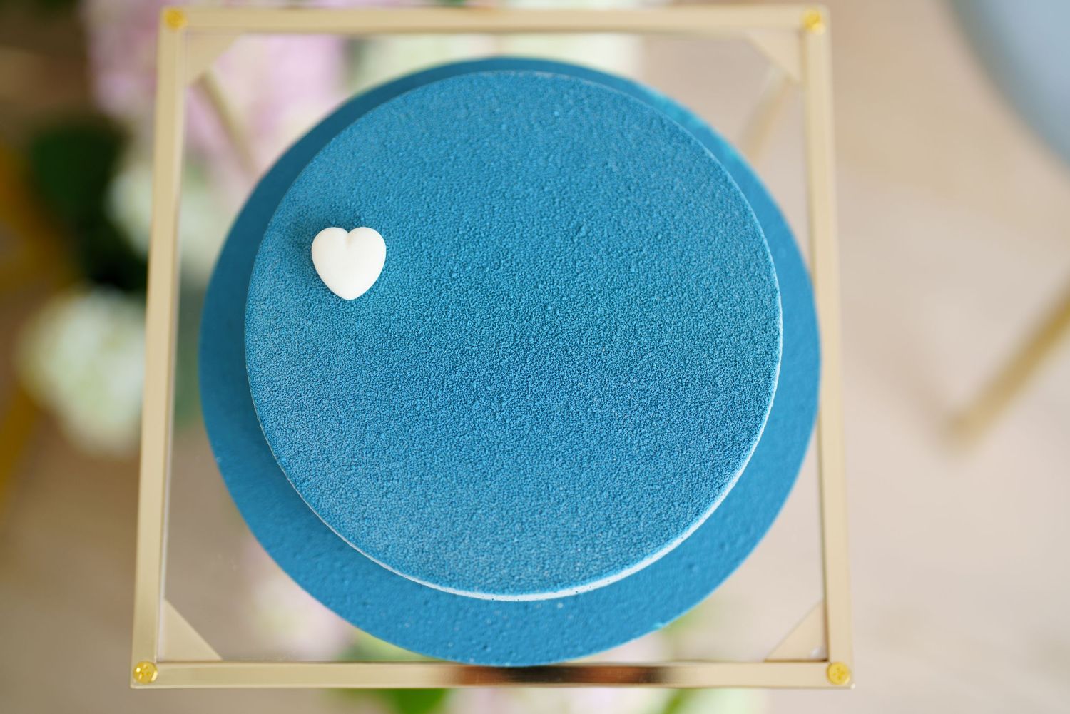 Blue velvet cake with white heart decoration on top, displayed on a gold-trimmed clear acrylic stand.