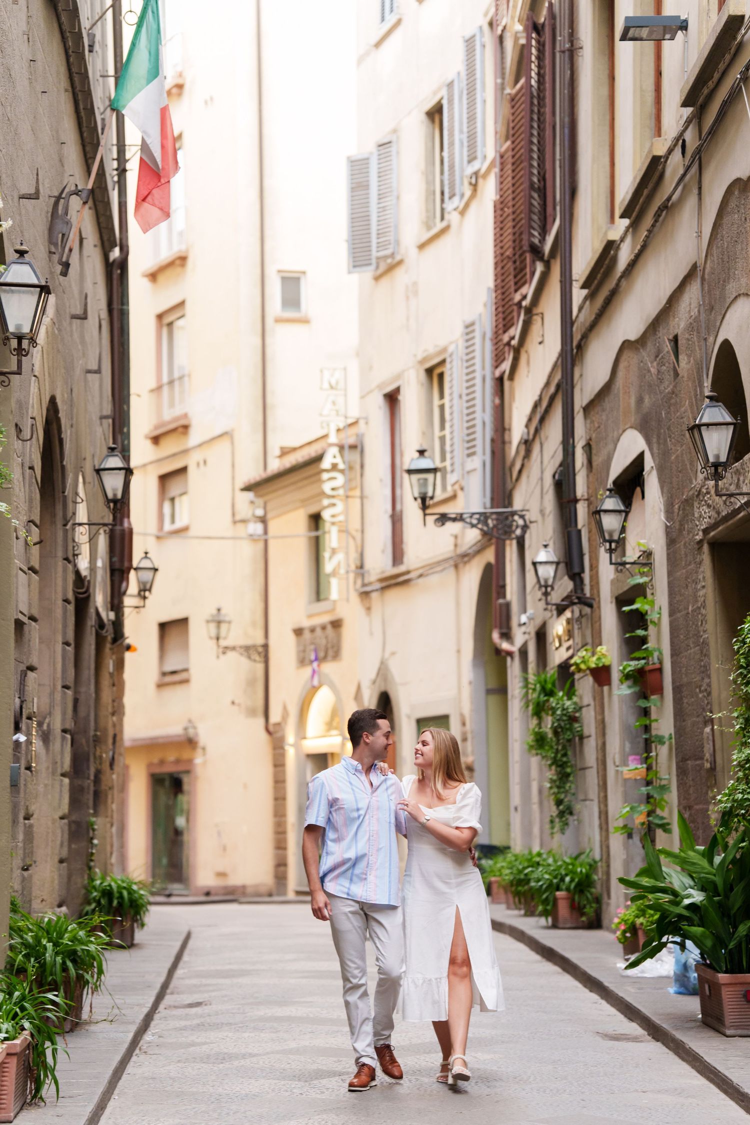 Couple walking hand in hand down a charming narrow cobblestone street in a European old town with historic buildings.