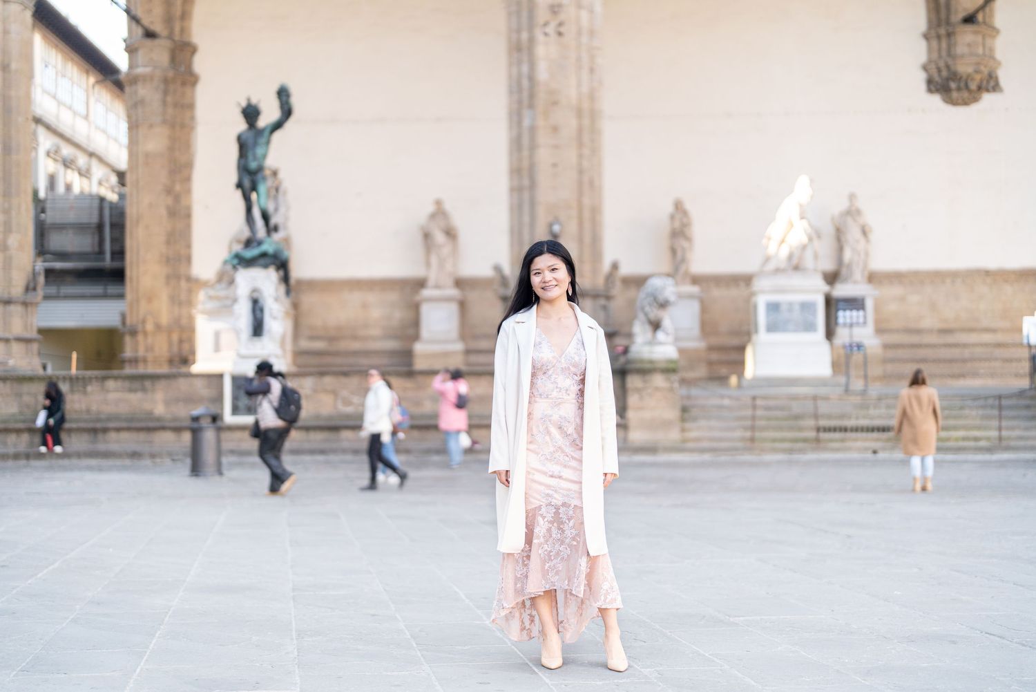 A person in a light pink outfit stands in front of historic statues at the Loggia dei Lanzi in Florence, Italy.