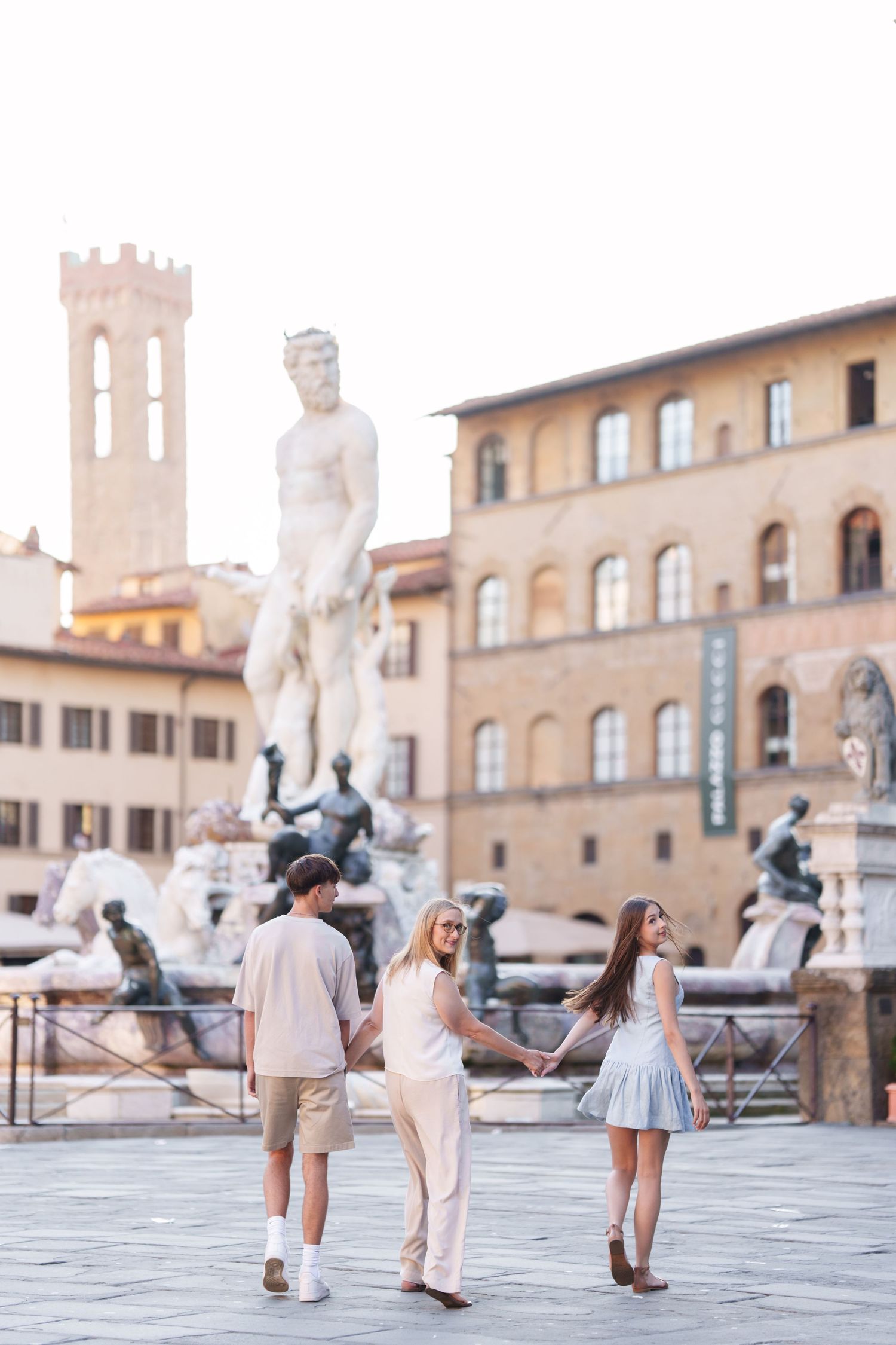 Tourists explore Piazza della Signoria in Florence, Italy with historic statues and architecture in background.