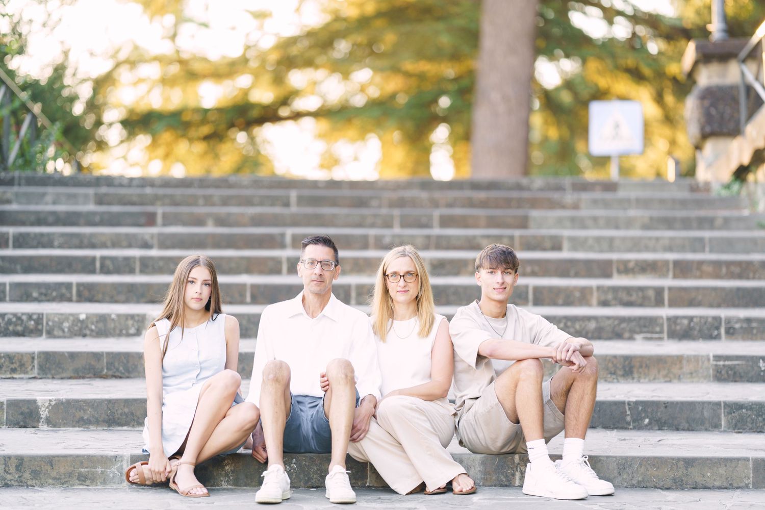 photographer Florence A group of young people in light colored casual clothing sit together on outdoor concrete steps on a sunny day.