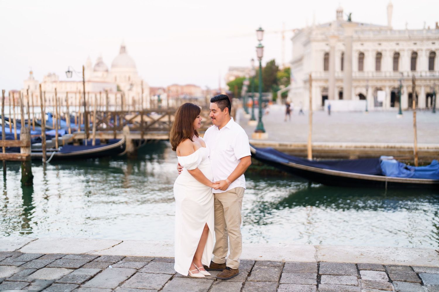 Romantic couple enjoys a tender moment on a stone walkway overlooking Venice's scenic canals and gondolas.