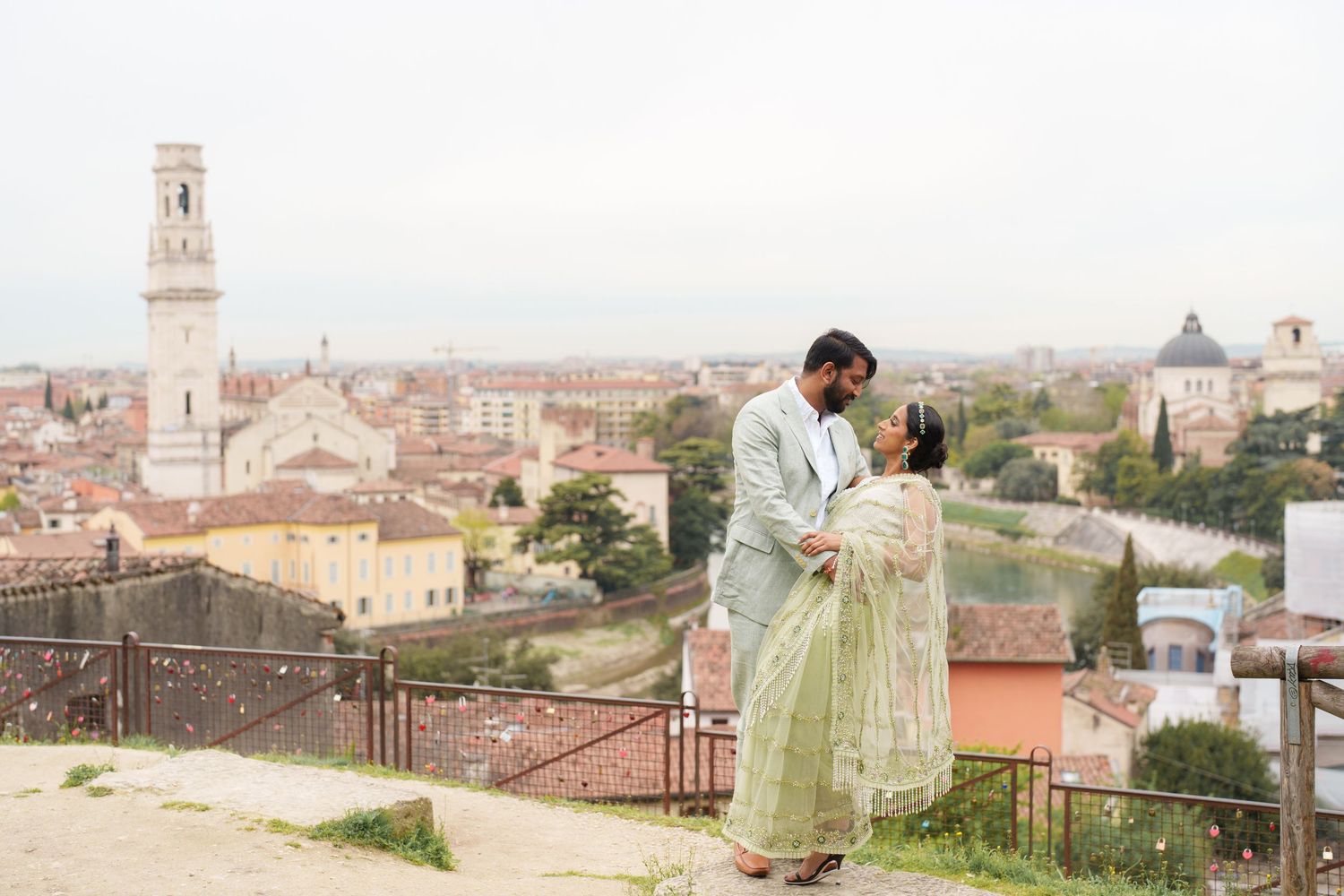 Romantic couple in elegant attire embraces on a scenic Italian terrace overlooking historic city rooftops and architecture.