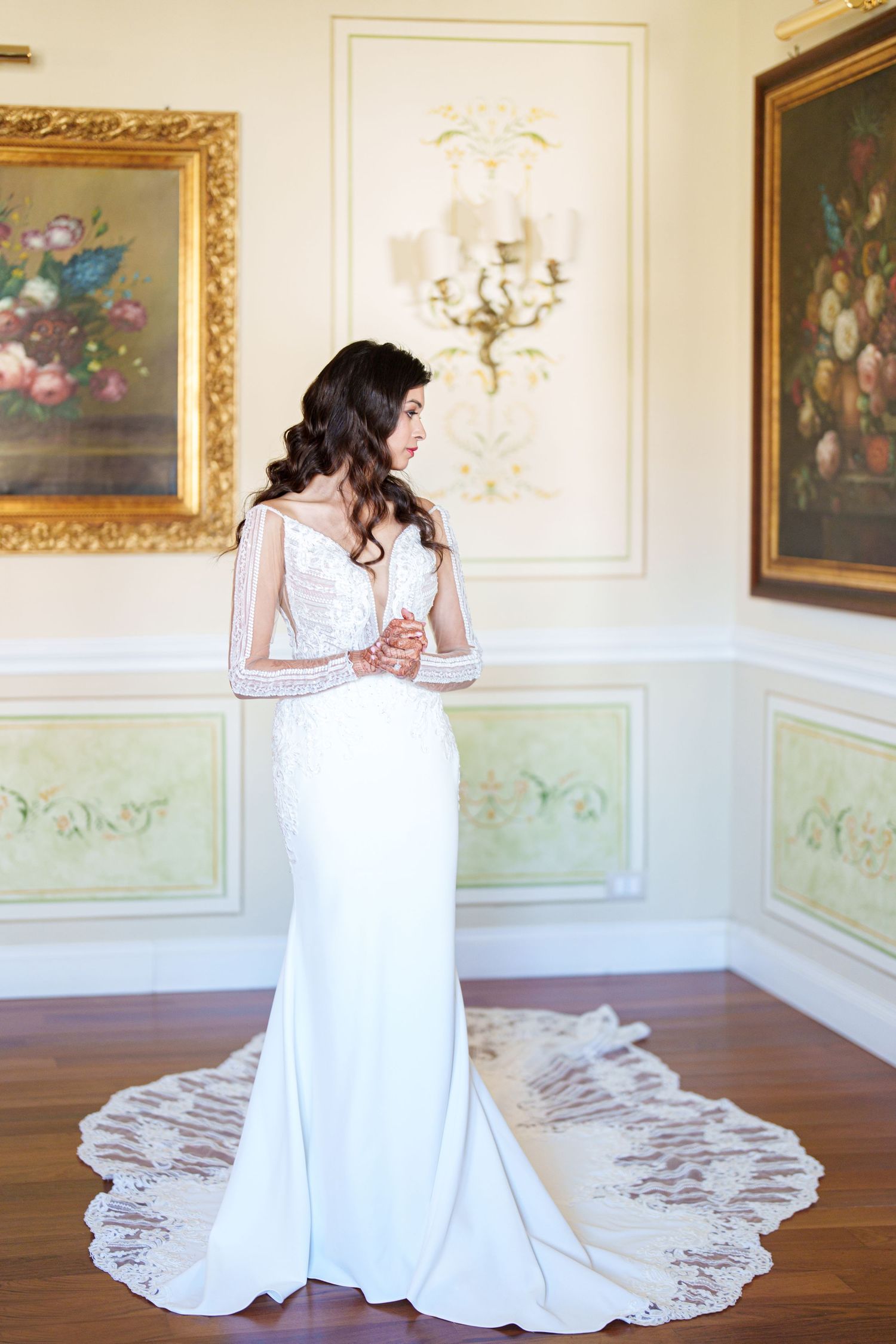 A bride in a flowing white dress poses gracefully in an elegant room with ornate gold-framed artwork on mint green walls.