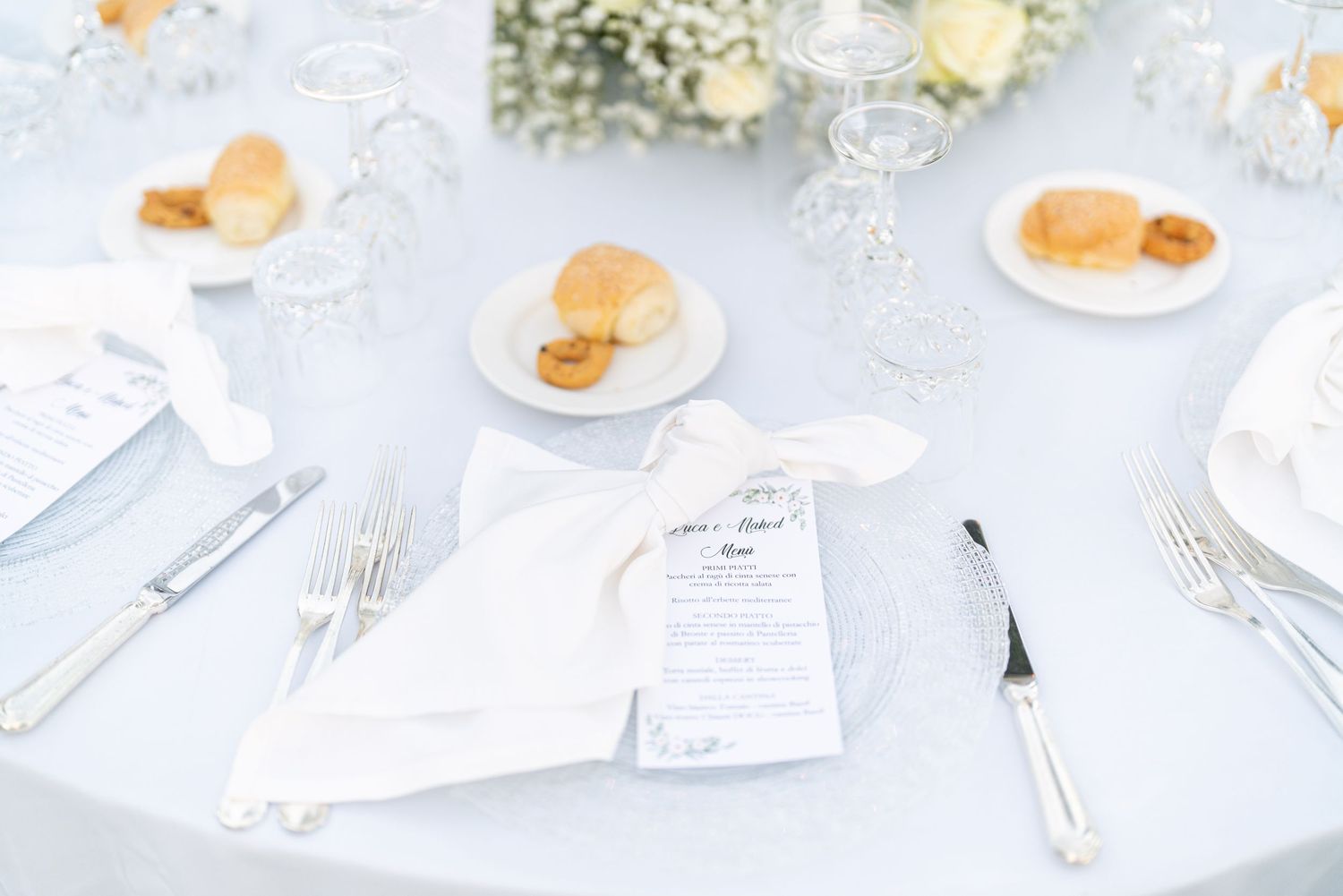 White table settings with menu cards and delicate floral arrangements at a wedding reception.